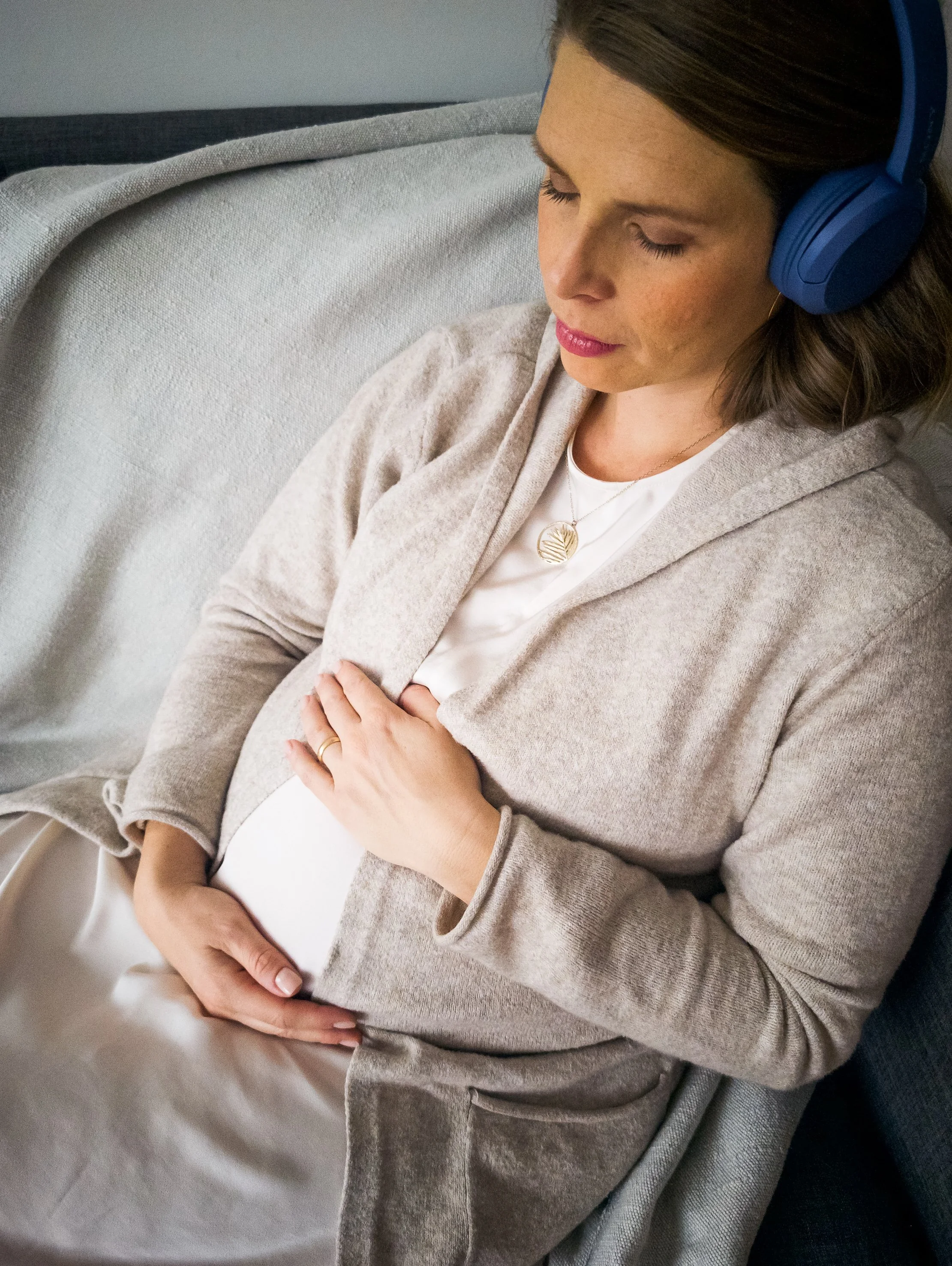 Verena resting on a couch with headphones on, listening to relaxation recordings with hand on her belly.