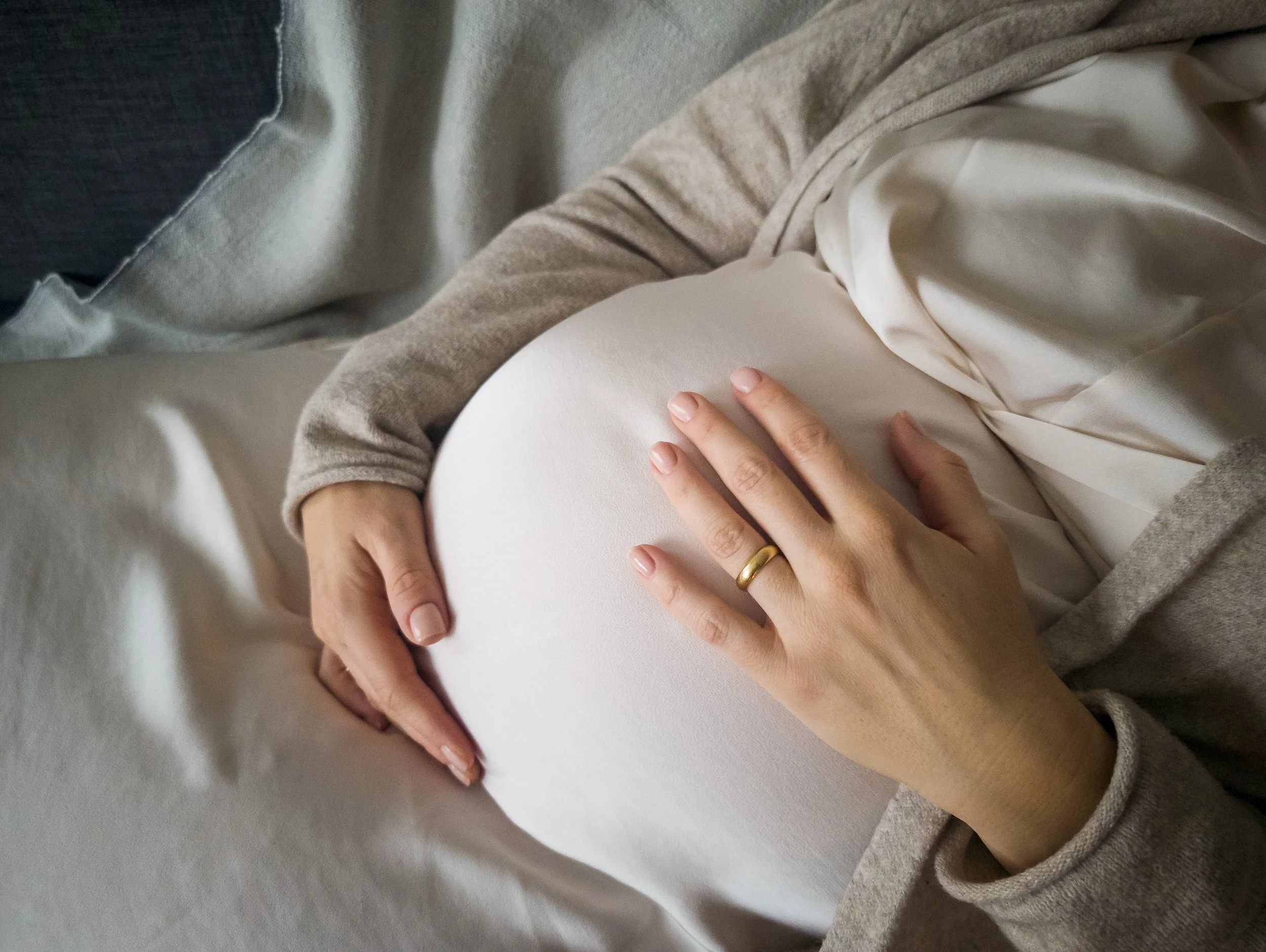 A pregnant woman lying on a bed, holding her belly with her hands.