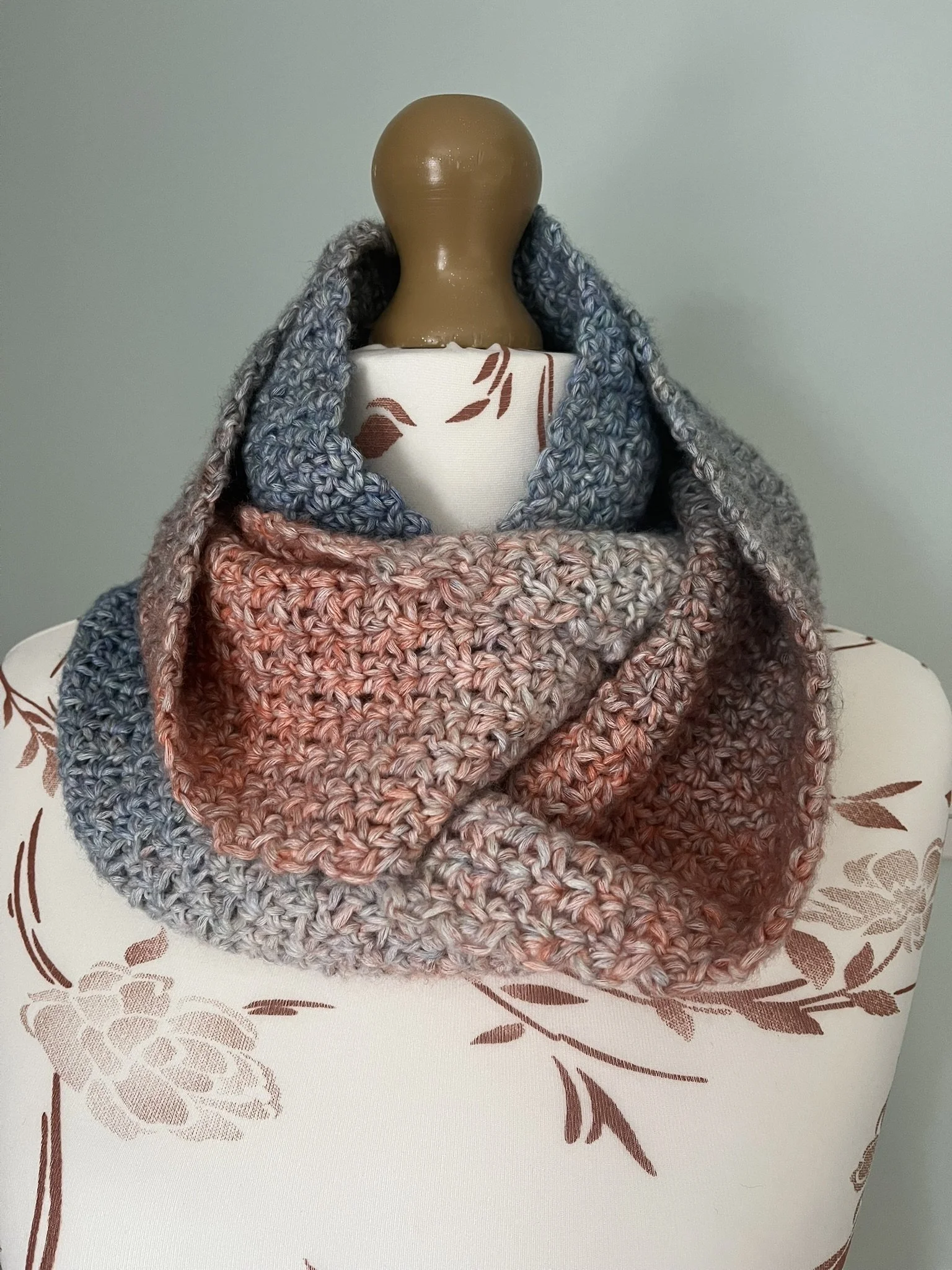 Handmade crochet infinity scarf in blue and coral colours wrapped around a mannequin