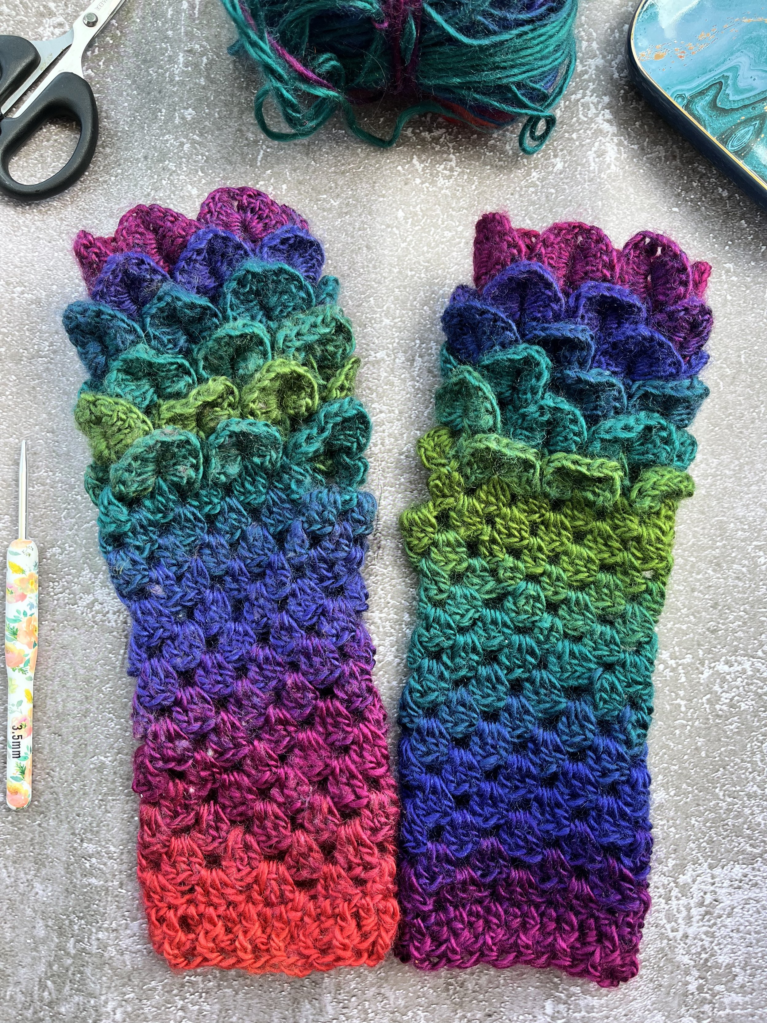 A uniques pair of handmade crochet dragon scale type fingerless gloves in unique blend of purple, blue, teal, green and red. One of a kind colour design