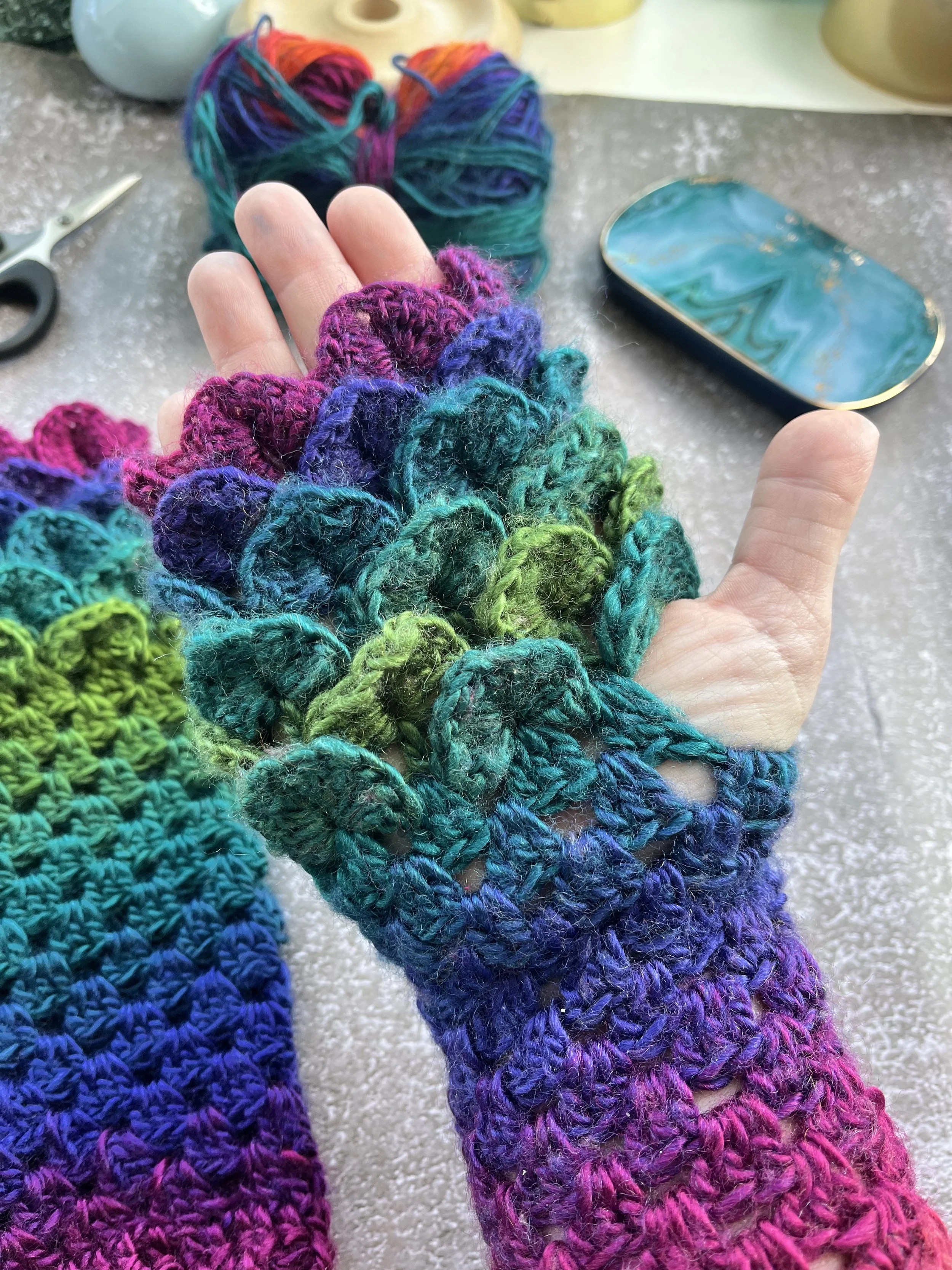 A uniques pair of handmade crochet dragon scale type fingerless gloves in unique blend of purple, blue, teal, green and red. Close up look at the dragon scale effect