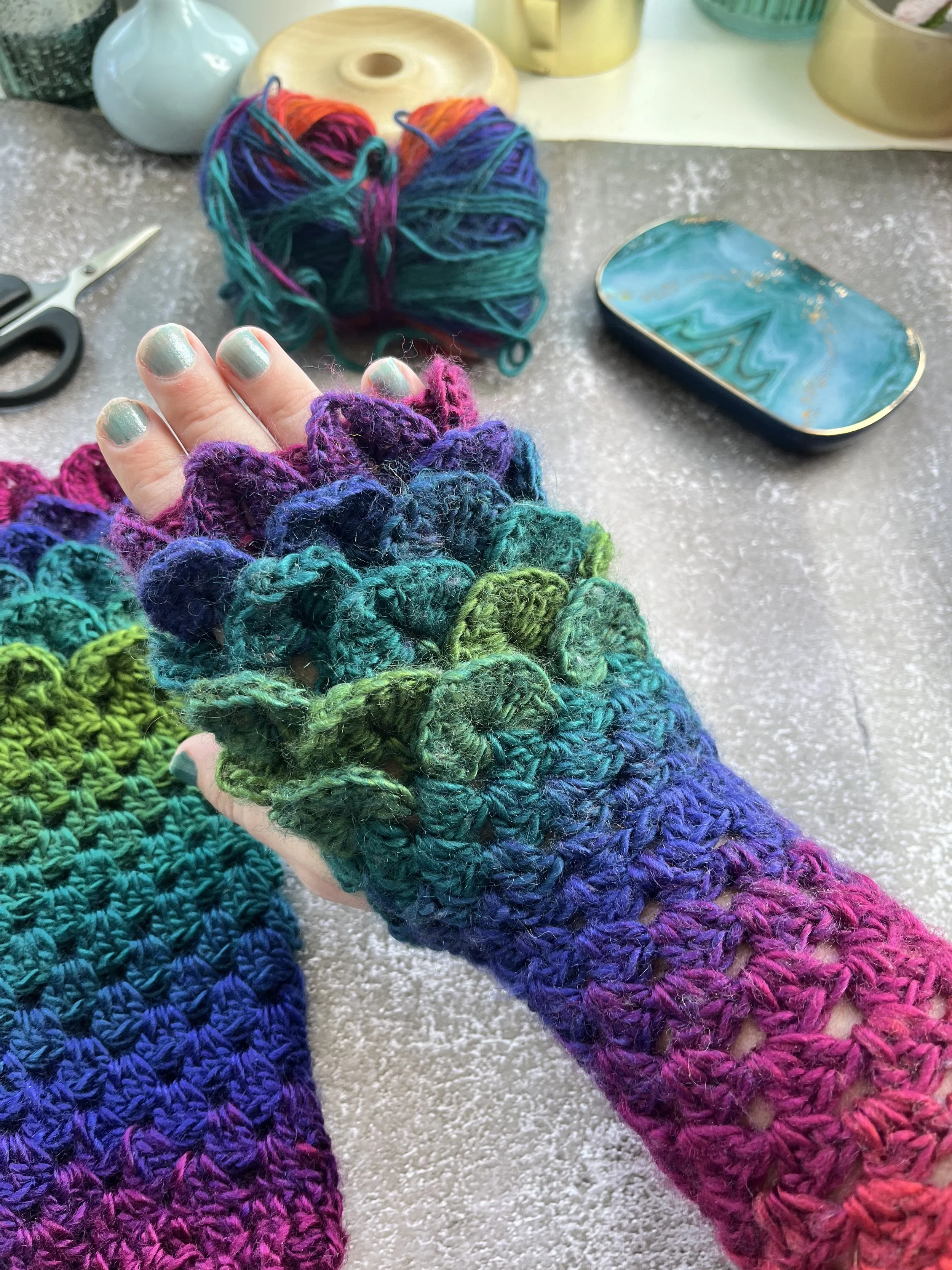 A uniques pair of handmade crochet dragon scale type fingerless gloves in unique blend of purple, blue, teal, green and red. One of a kind colour design