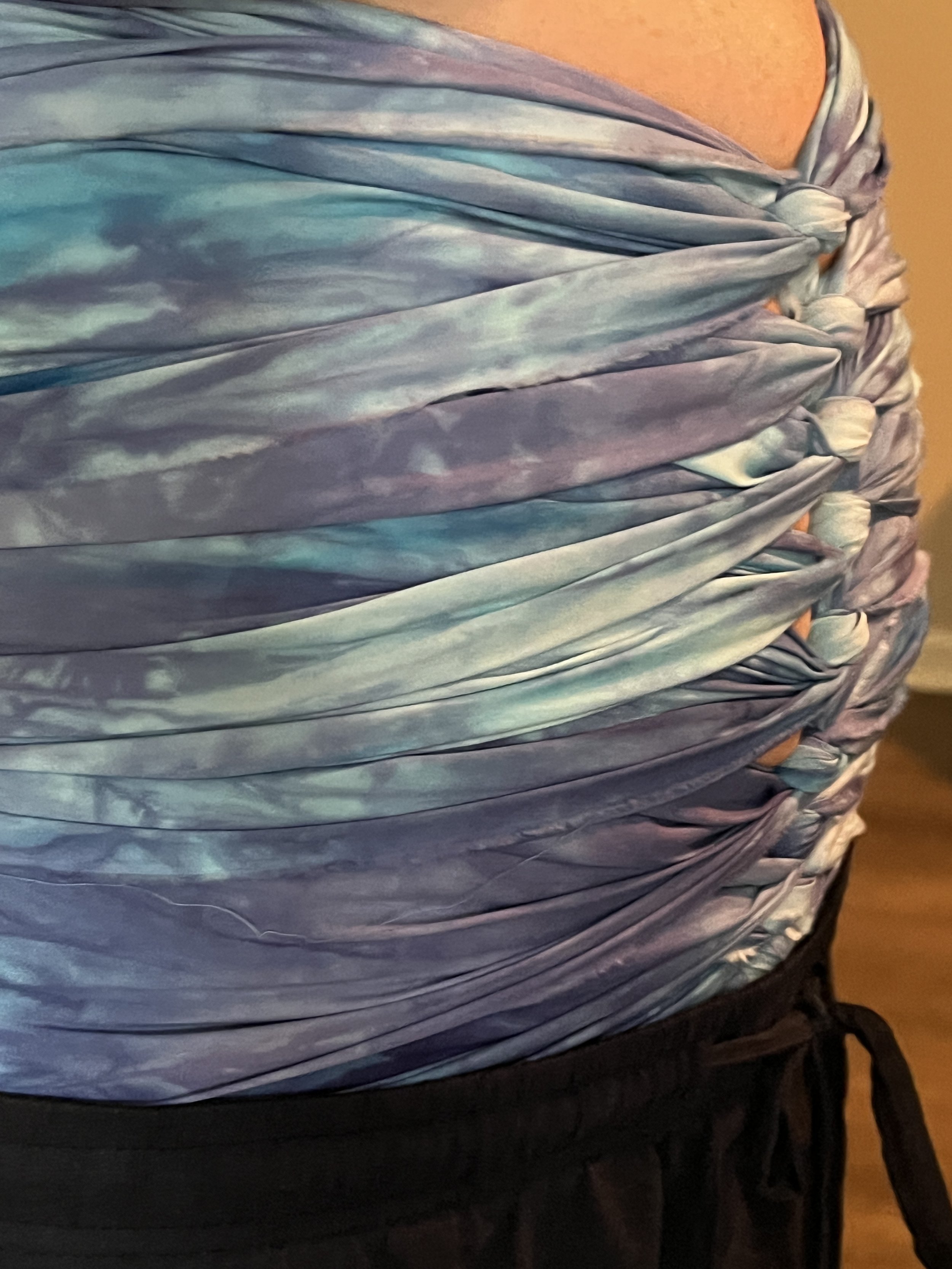Close-up of someone wearing a multicolored, twisted and gathered fabric top or dress in shades of blue, purple, and pink, paired with black drawstring pants.