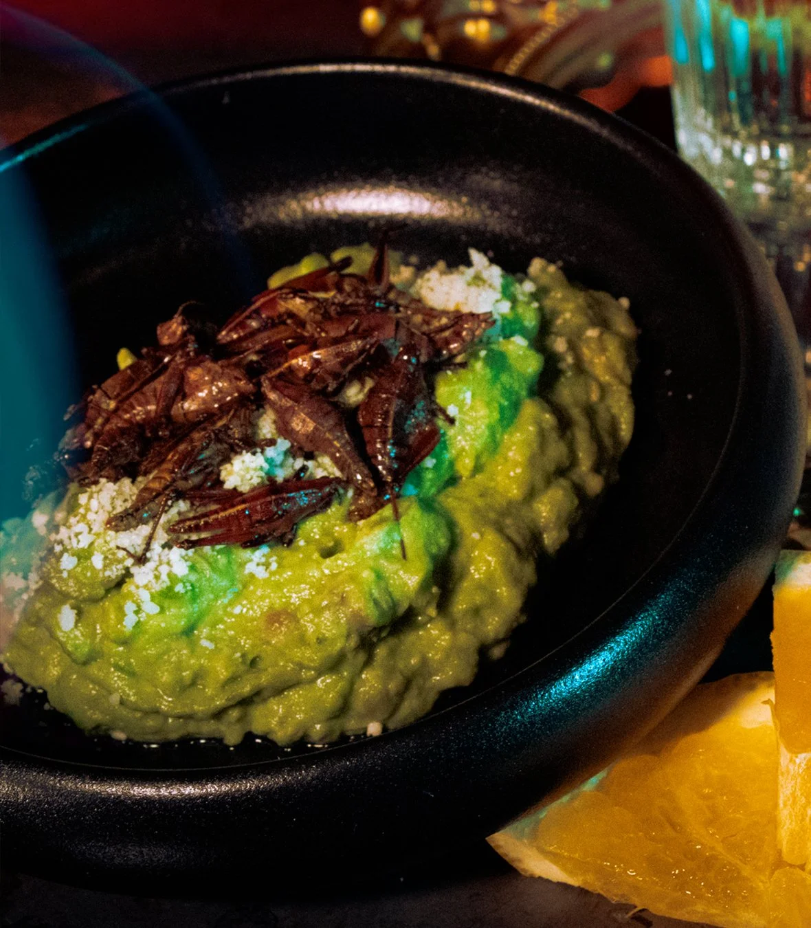 Guacamole topped with crickets in a black bowl, with orange slices beside it. sabina mezcaleria boston, food photography, professional photographer boston, Mexican restaurant boston