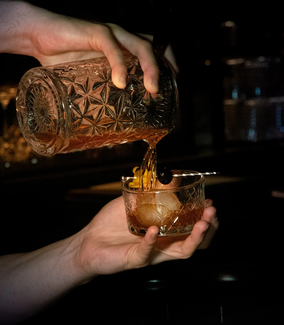 Person pouring whiskey cocktail into glass with ice and garnish, sabina mezcaleria marketing, food photography Boston, professional photographer Boston. aesthetic, elegant photography, dark aesthetic