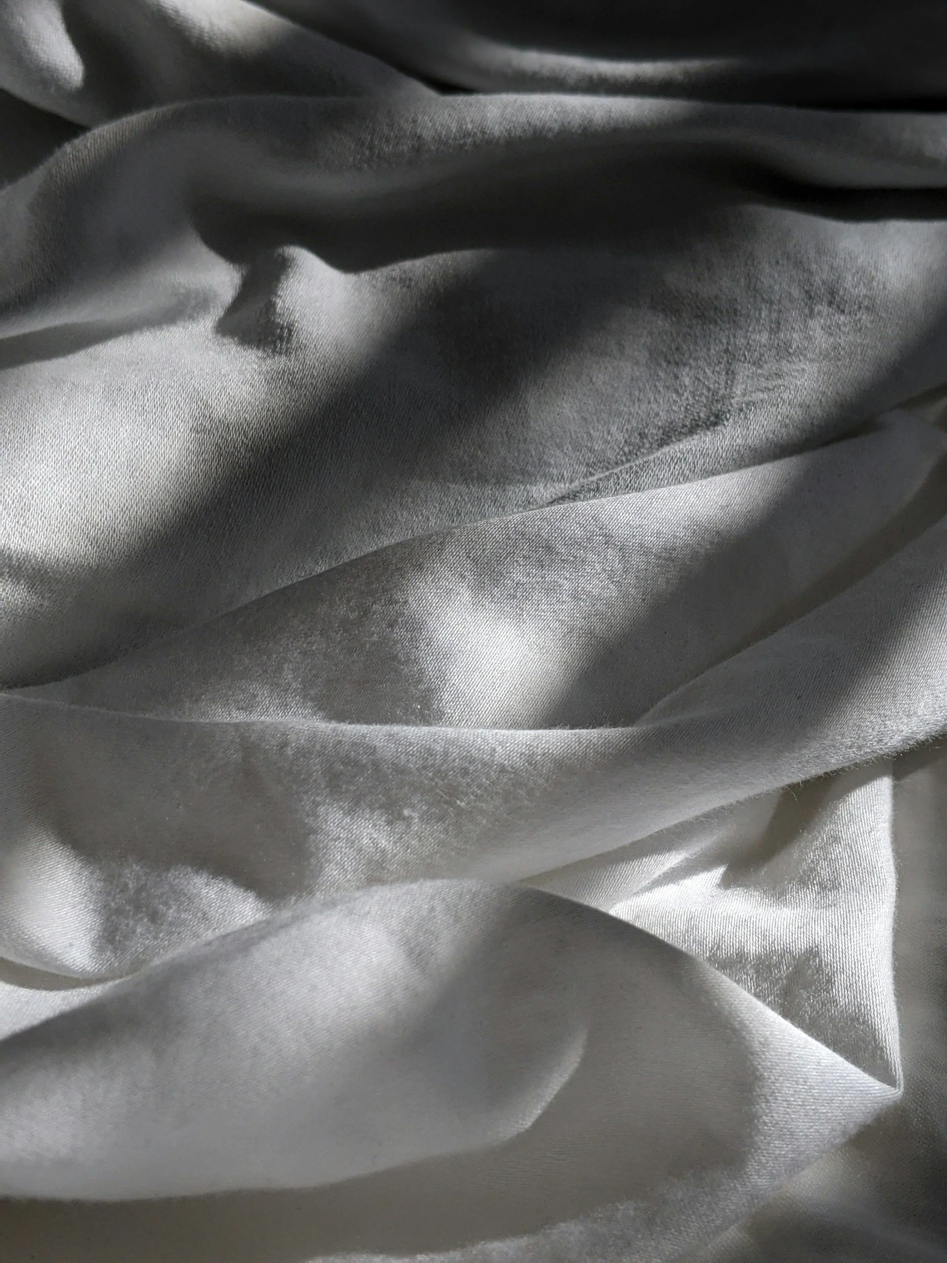 Close-up of light gray silk fabric with folds and sheen.