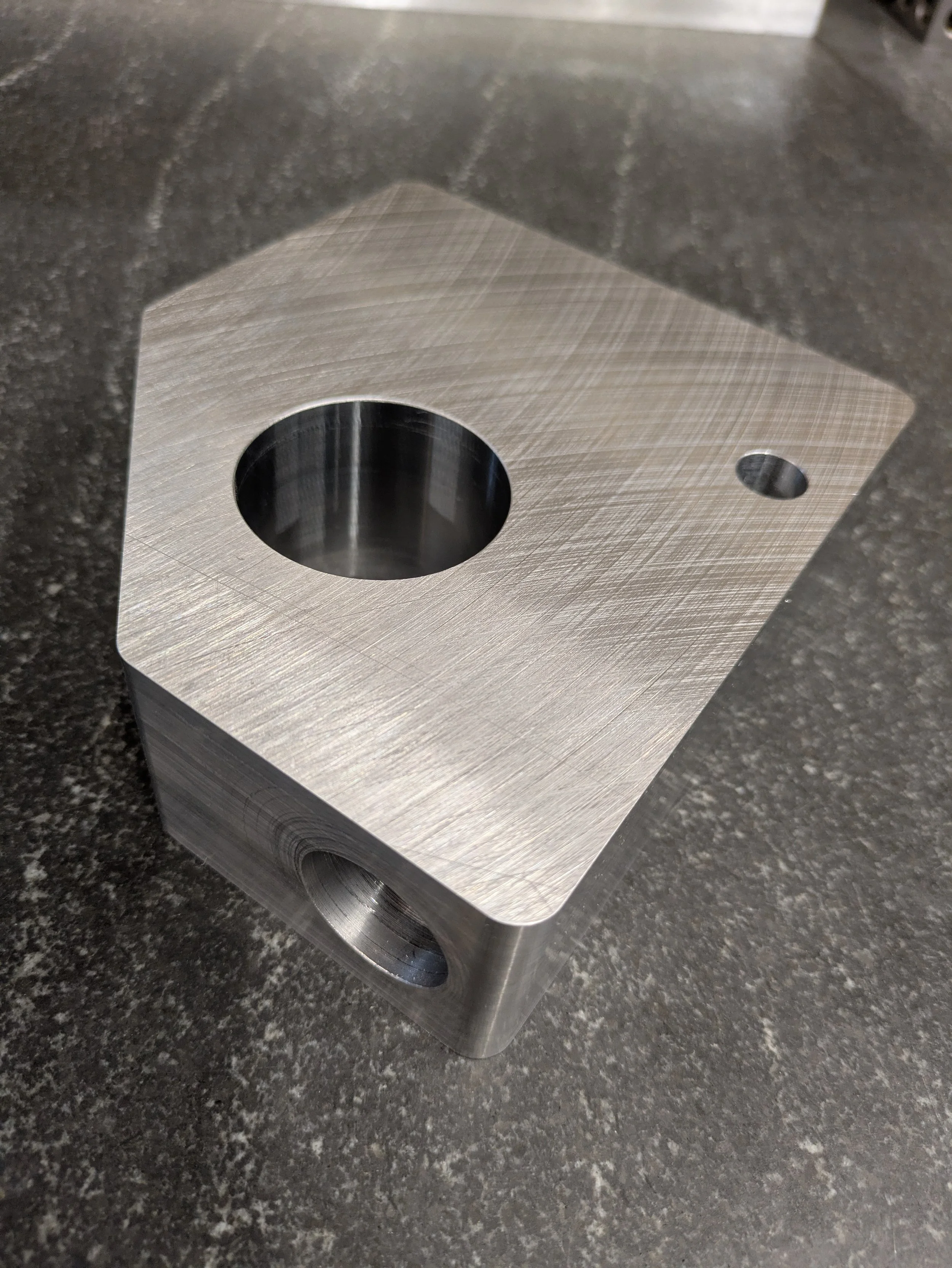 A stack of rectangular metal plates with a large circular hole and a smaller hole on each plate, sitting on a dark speckled countertop.