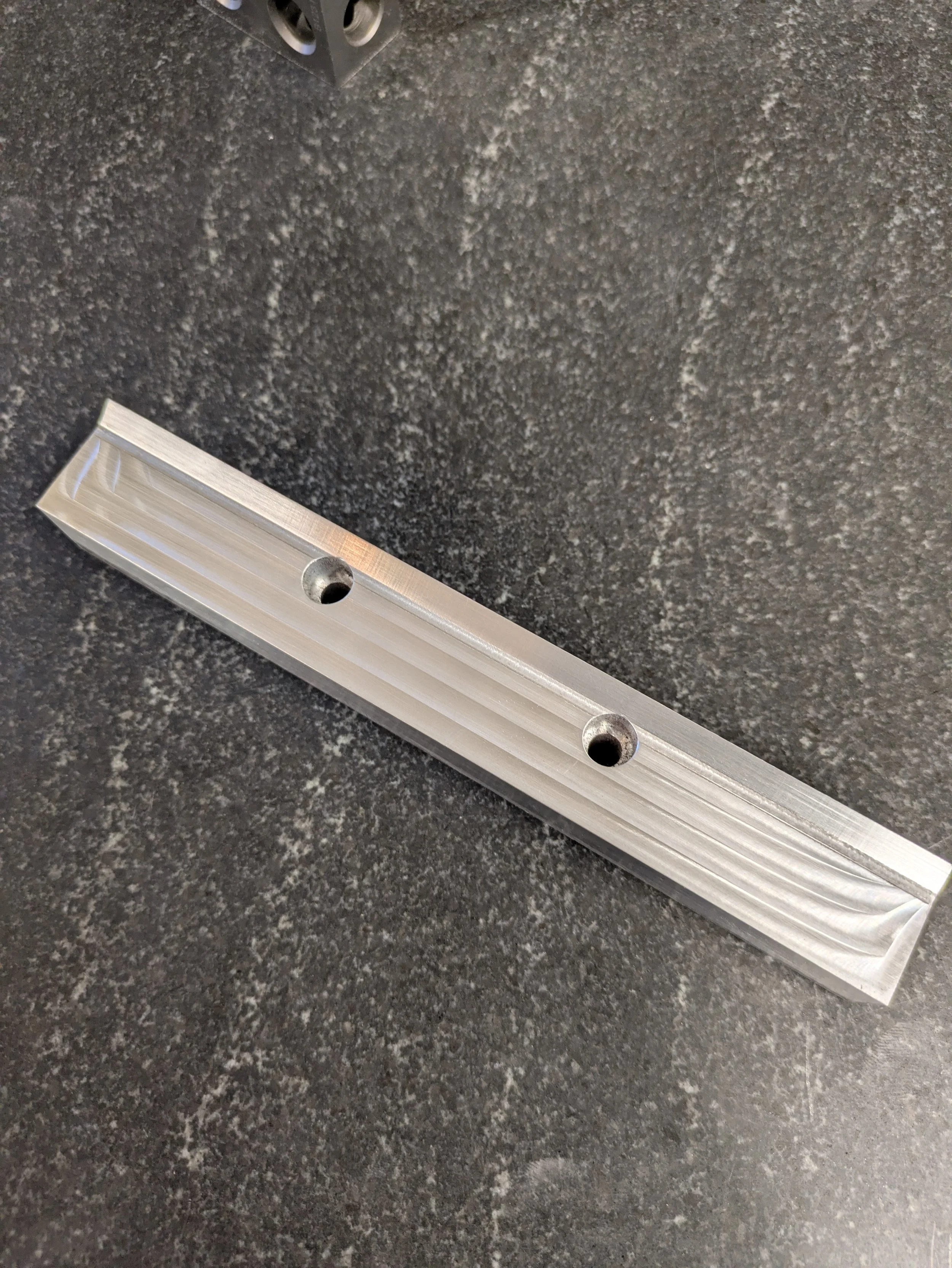 A close-up image of a textured dark gray countertop with a metal level tool placed on it and a small metal container in the upper left corner.