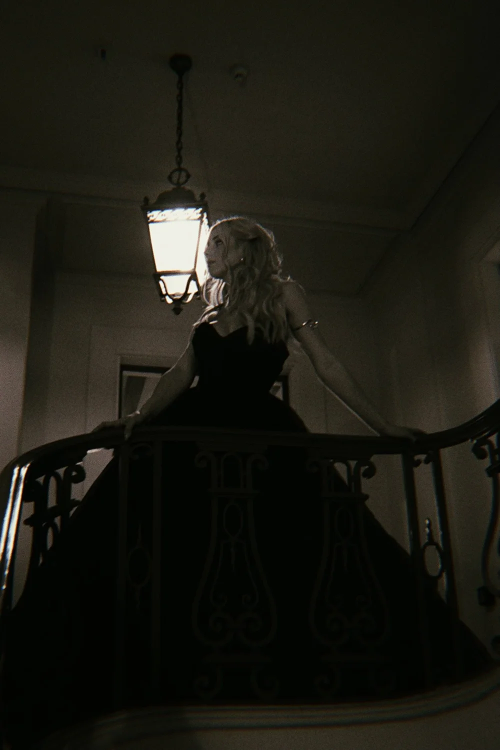 Zoe in a black dress on a balcony beneath a hanging lantern