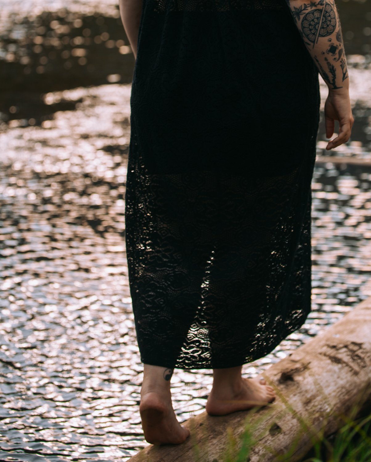 Jessica Huss walking on a log with water in the background, wearing a black lace dress