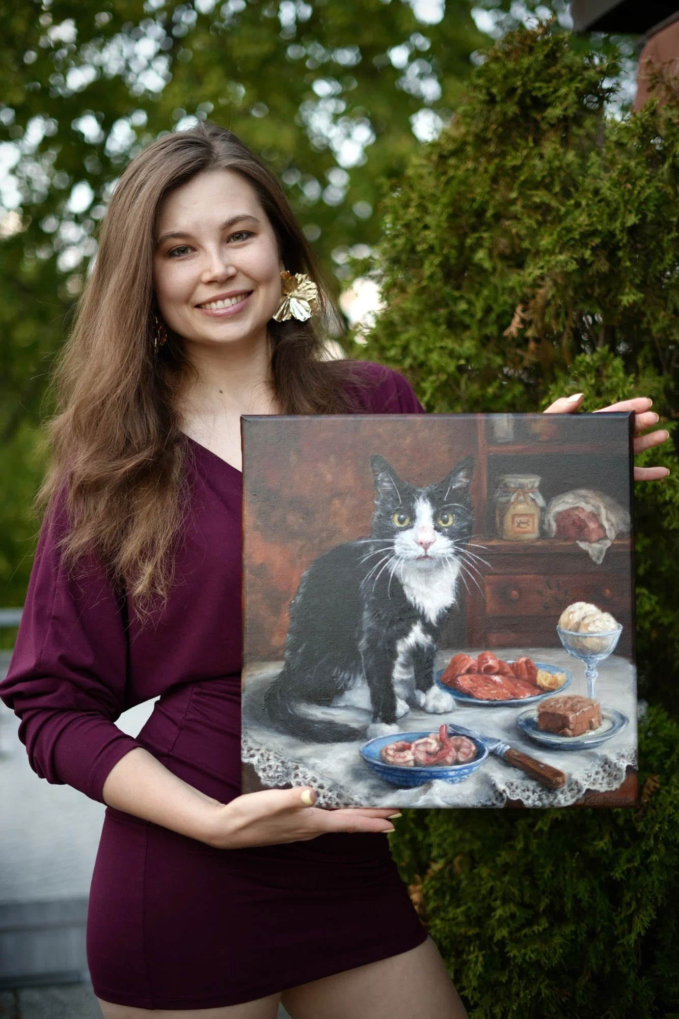 Artist Katerina Akhmylova holding a finished cat still-life oil painting outdoors, smiling