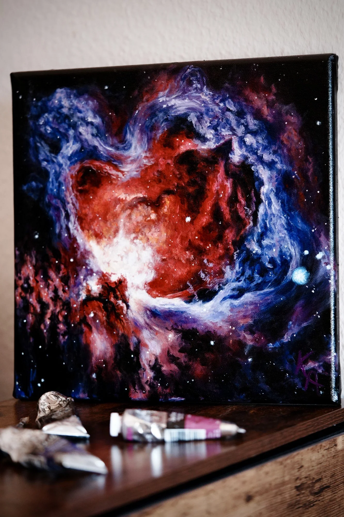 Glow-in-the-dark nebula oil painting on canvas, angled view in daylight showing red and blue nebula clouds