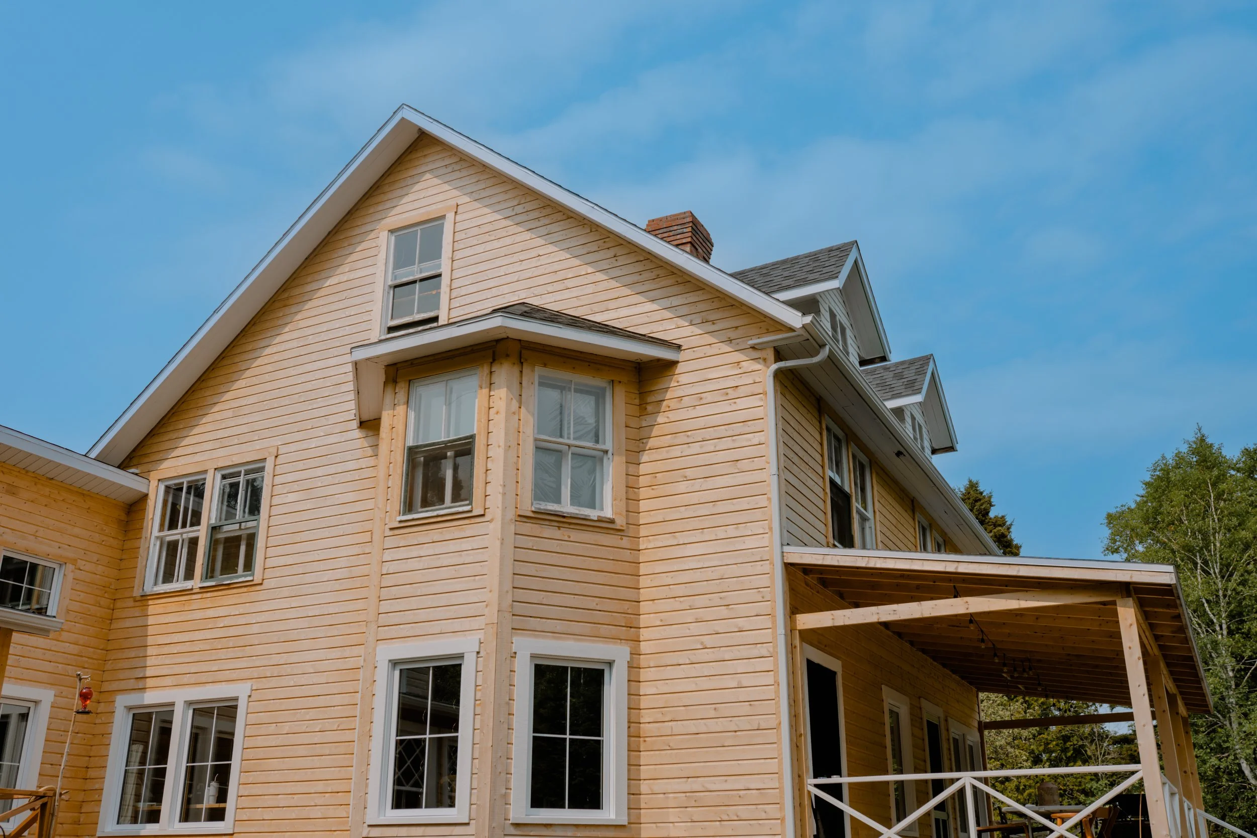 Maison en bois en construction avec fenêtres, porche, et toit en pente sous un ciel bleu.