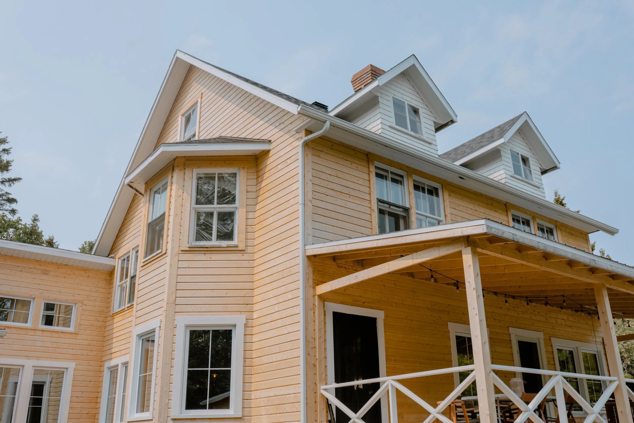 Maison en bois à plusieurs étages avec un porche et plusieurs fenêtres, sous un ciel clair.