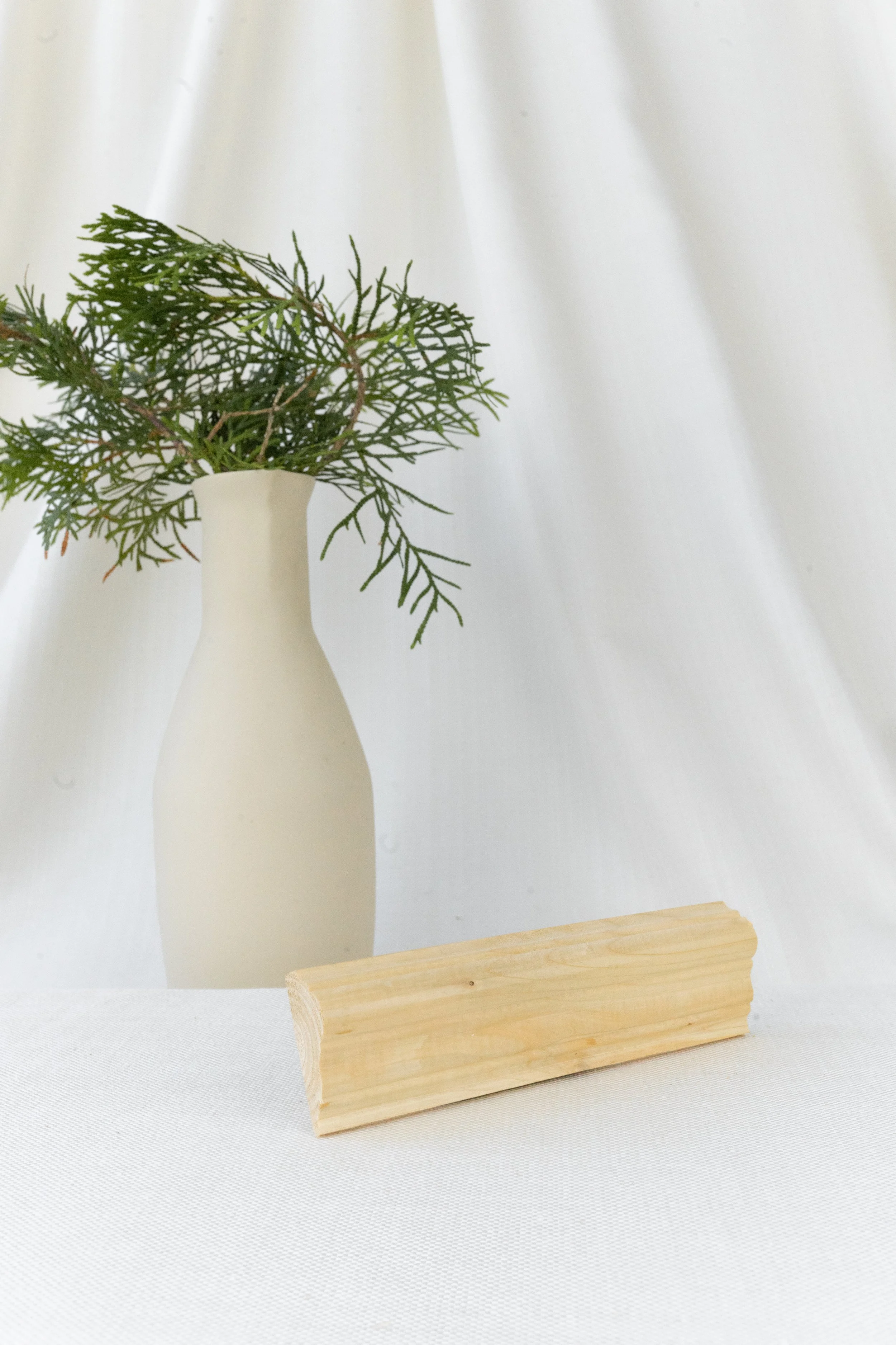 Vase blanche avec des branches de feuillage vert, fond blanc, surface en tissu blanc.