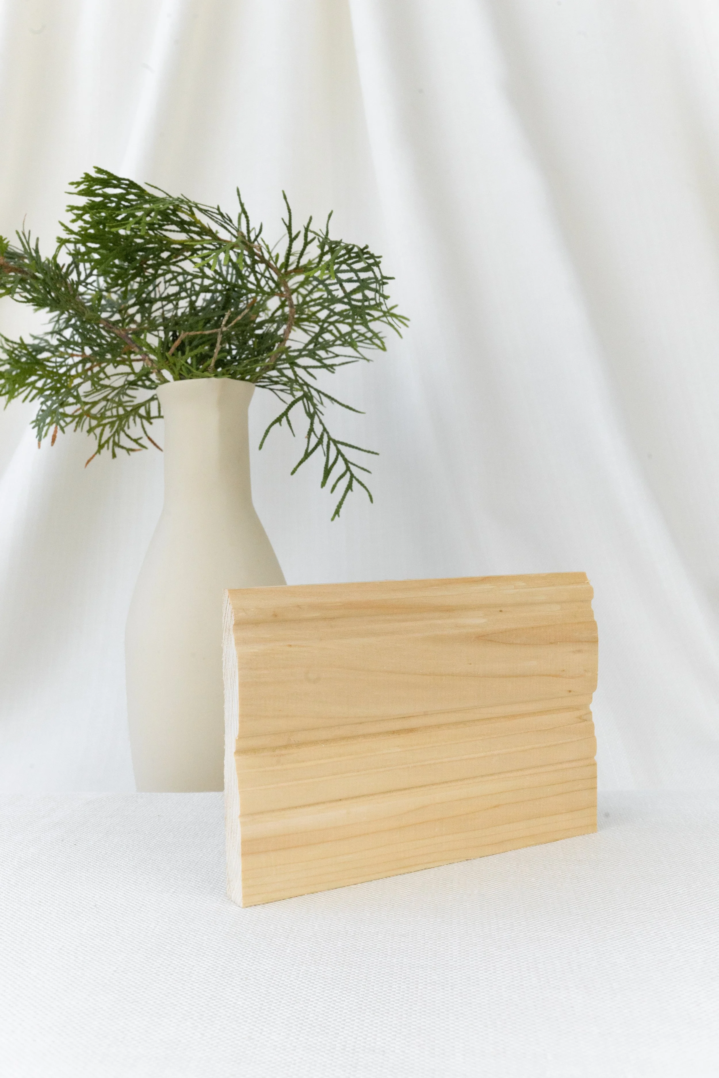Vase blanc avec des branches vertes et un morceau de bois naturel sur un fond blanc.