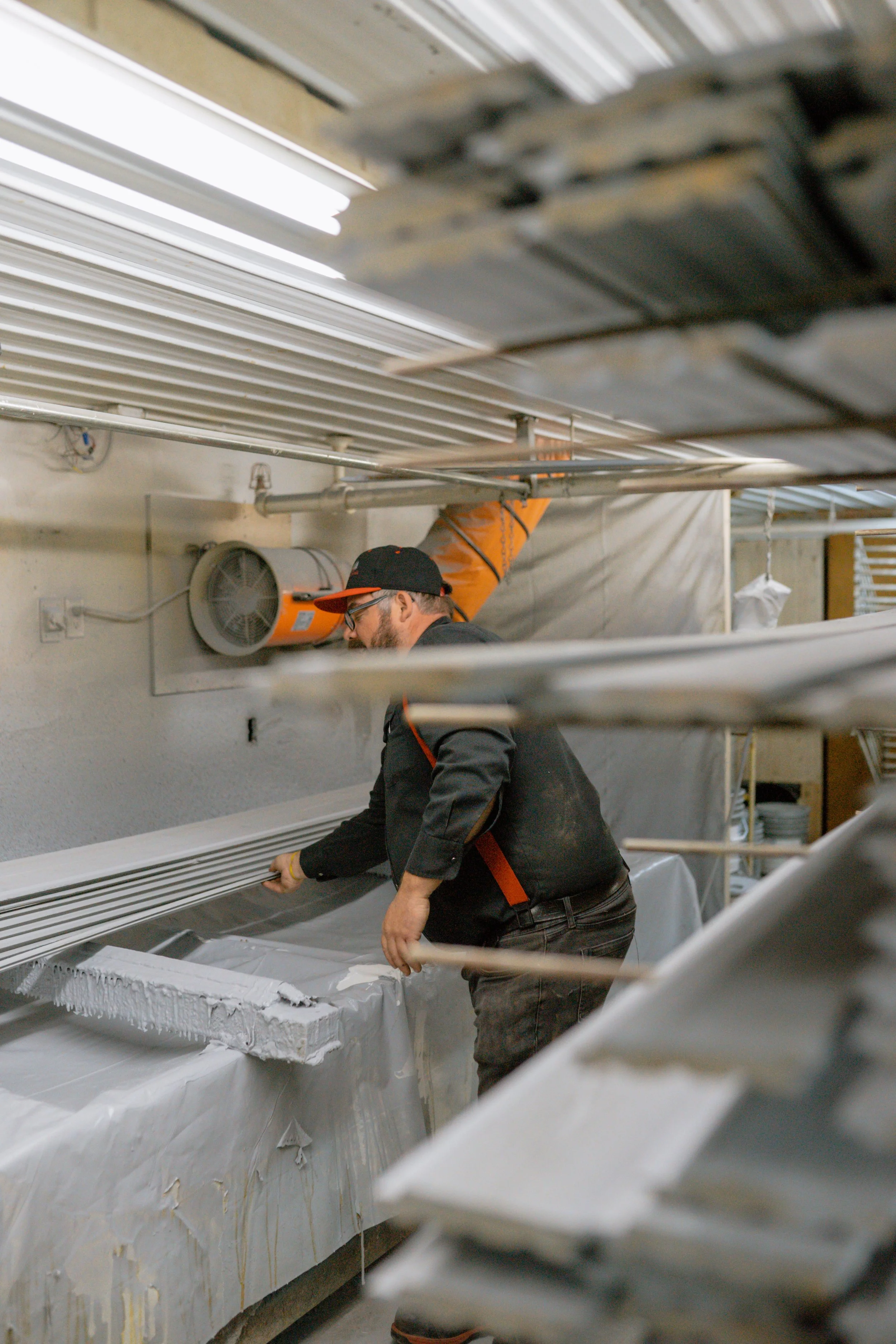 Un homme travaillant dans une fabrique de panneaux de mousse, positionné devant une machine de fabrication, entouré de différentes pièces métalliques.