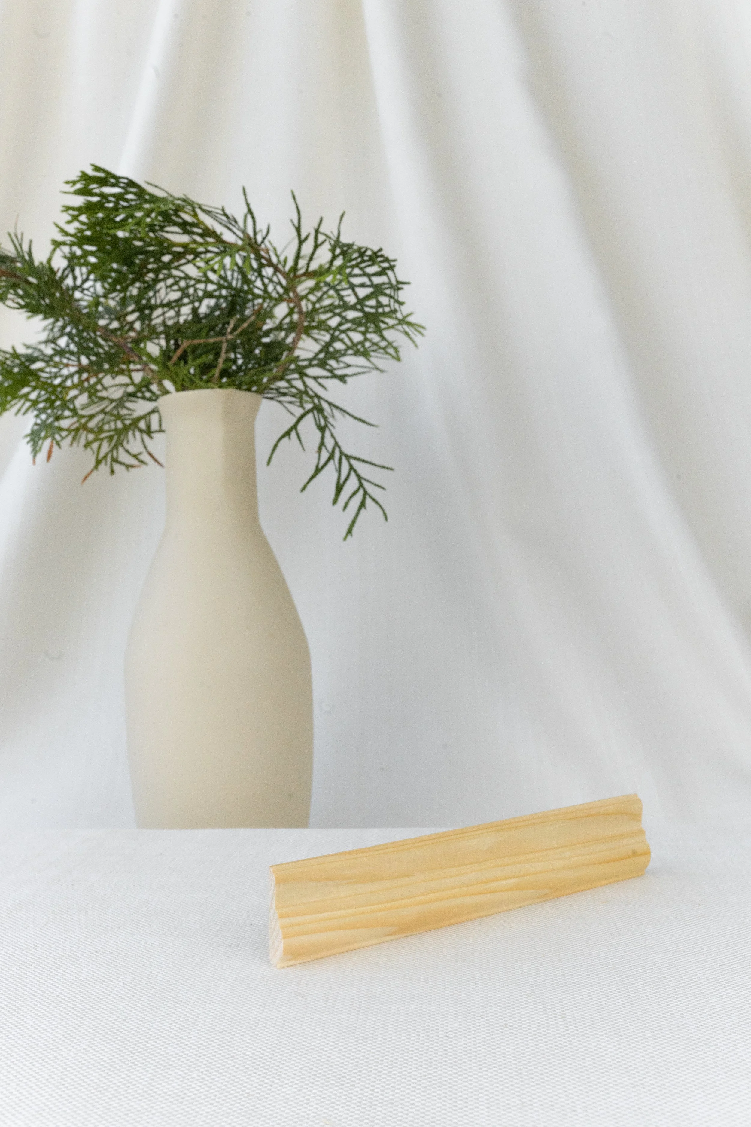 Vase blanche avec des branches vertes et une pièce de bois clair en premier plan, fond blanc