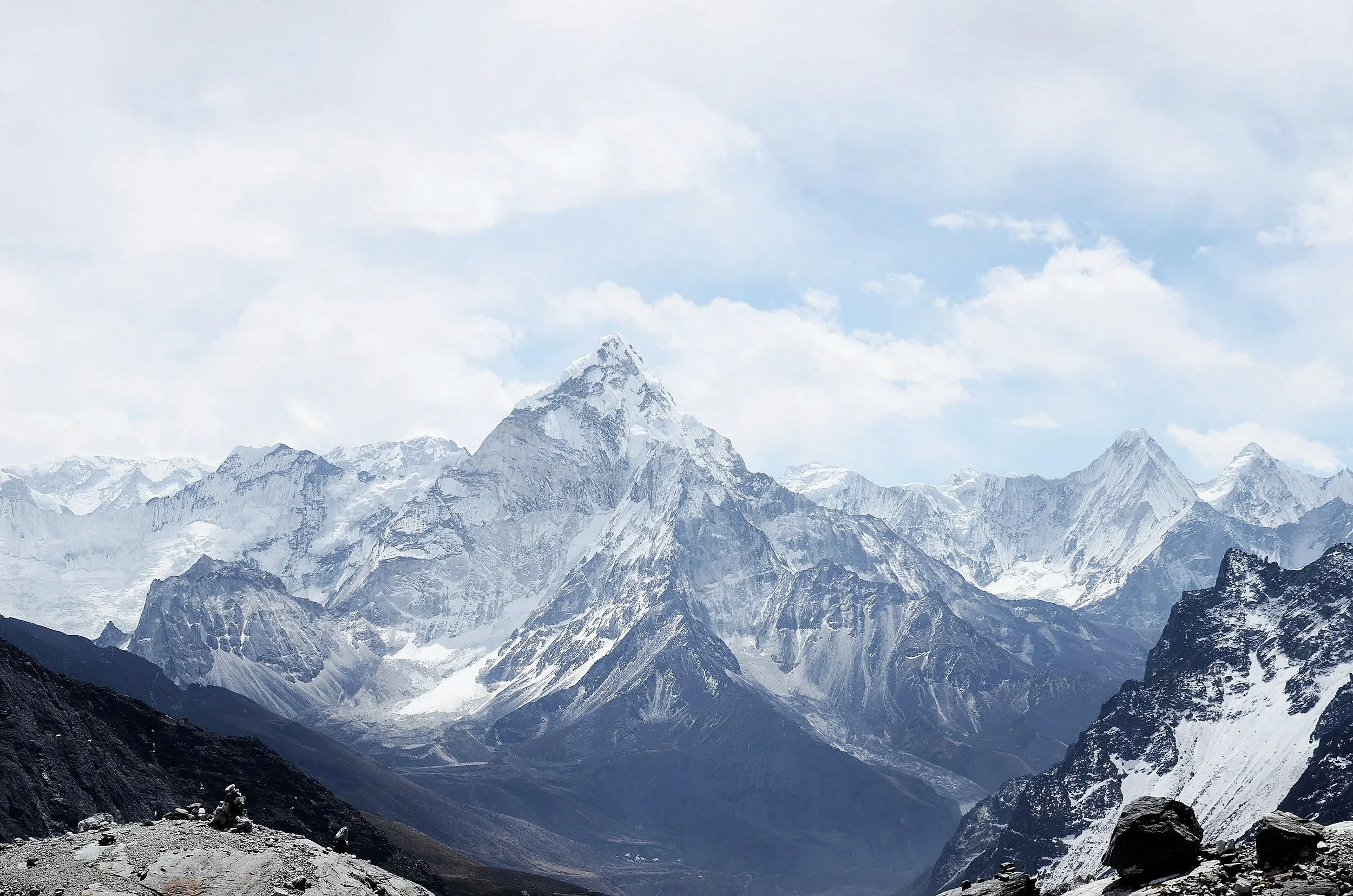 Snow-capped mountains under cloudy sky with rocky foreground.