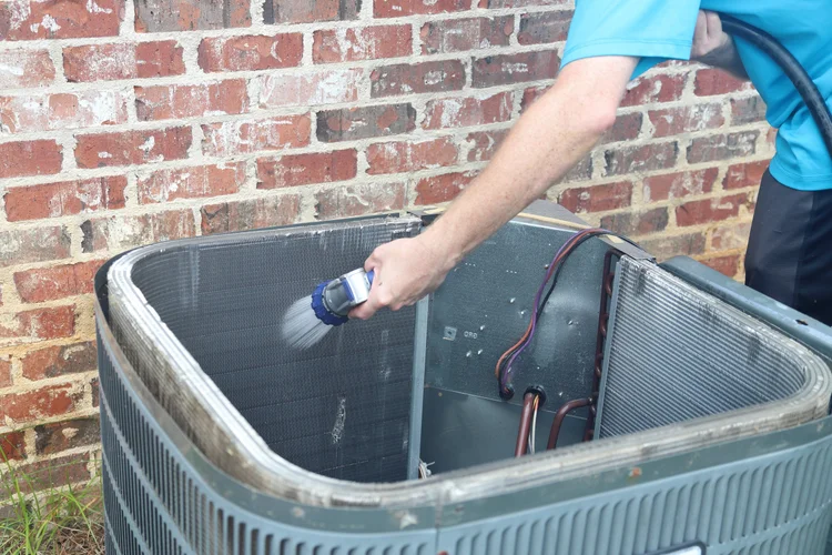 Technician cleaning an air conditioner condenser coil for improved efficiency and performance