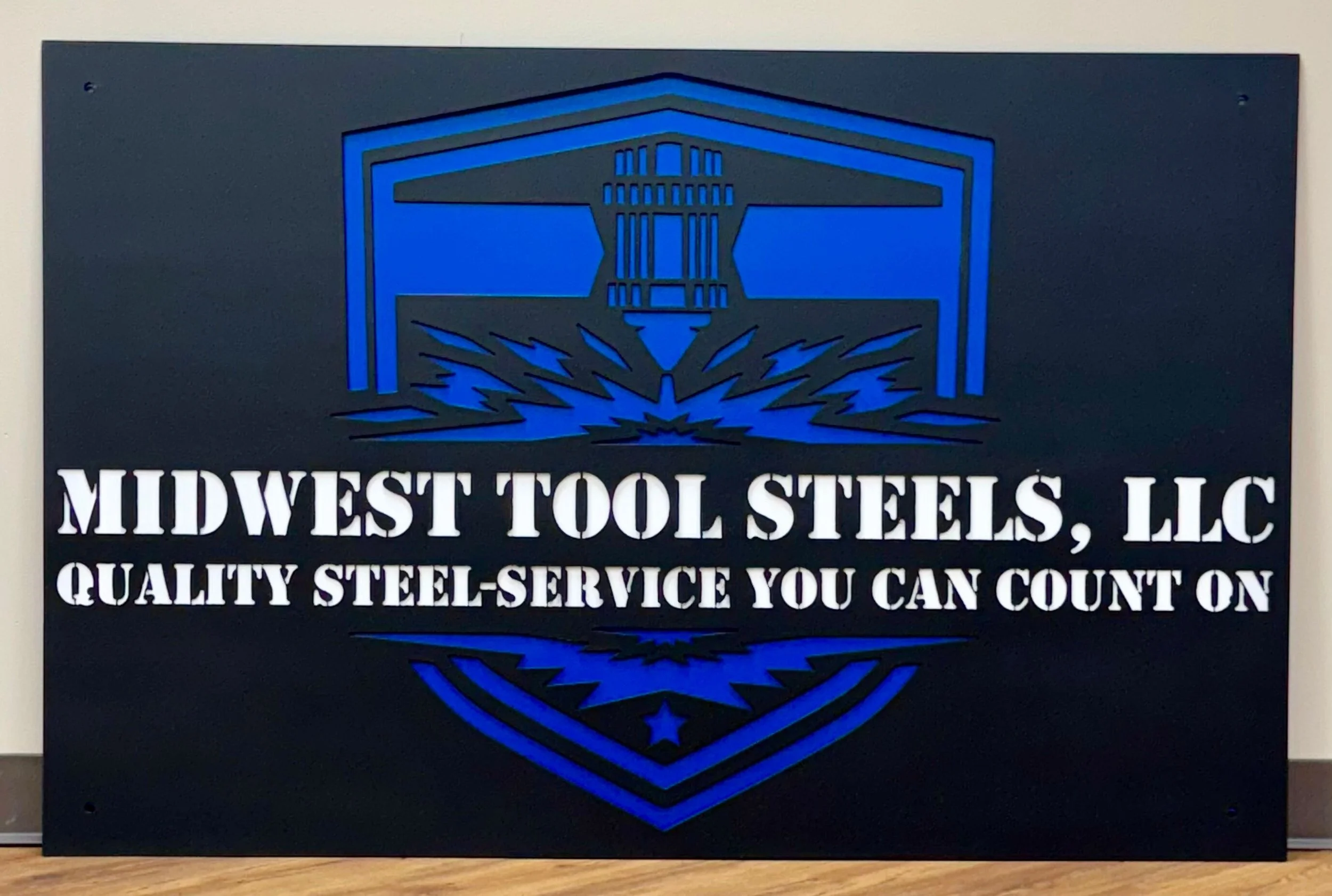 Black and blue sign for Midwest Tool Steels LLC with a graphic of a steel mill and the text, "Quality Steel - Service You Can Count On."