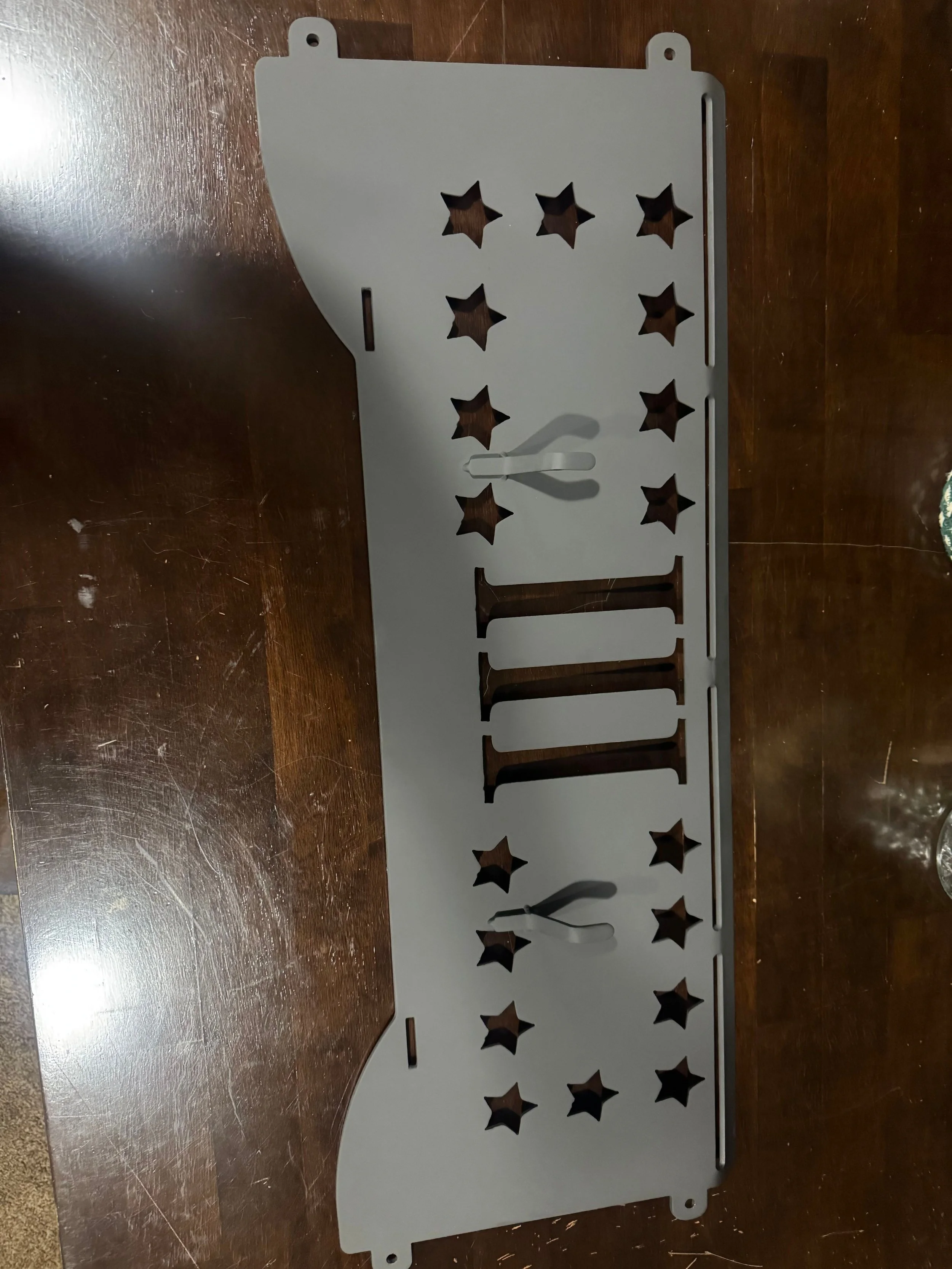 A metal wall-mounted rack decorated with cutouts of stars and Roman numerals, used as a clock with adjustable clock hands.