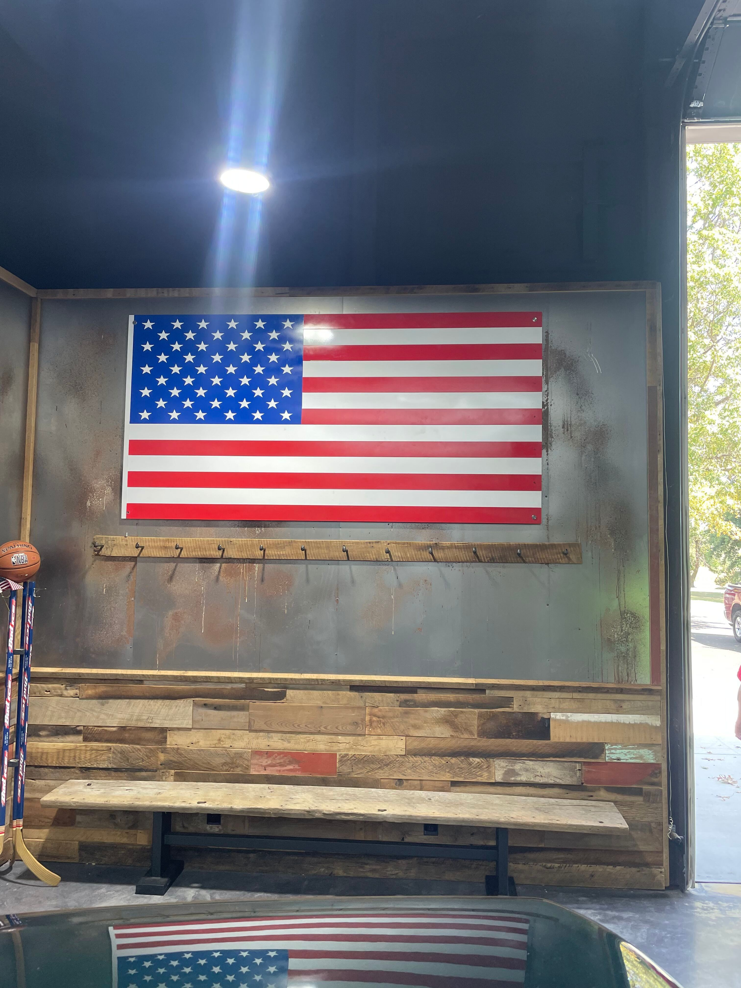 American flag hanging on a wall inside a garage or workshop with a wooden bench below.
