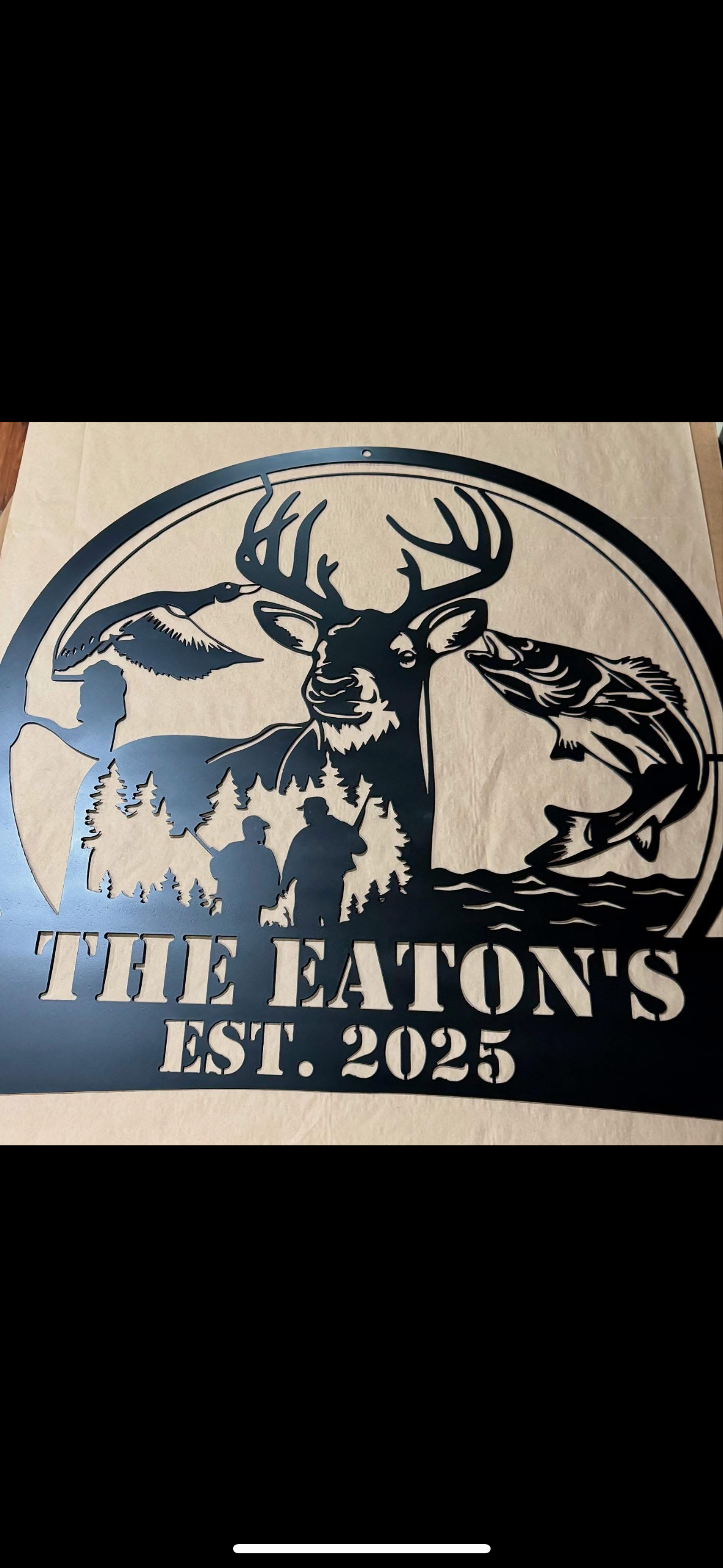 Metal outdoor sign featuring a buck deer with large antlers, a flying bird, a fisherman catching a fish, and the water and forest landscape. Text reads 'THE EATON'S EST. 2025'.