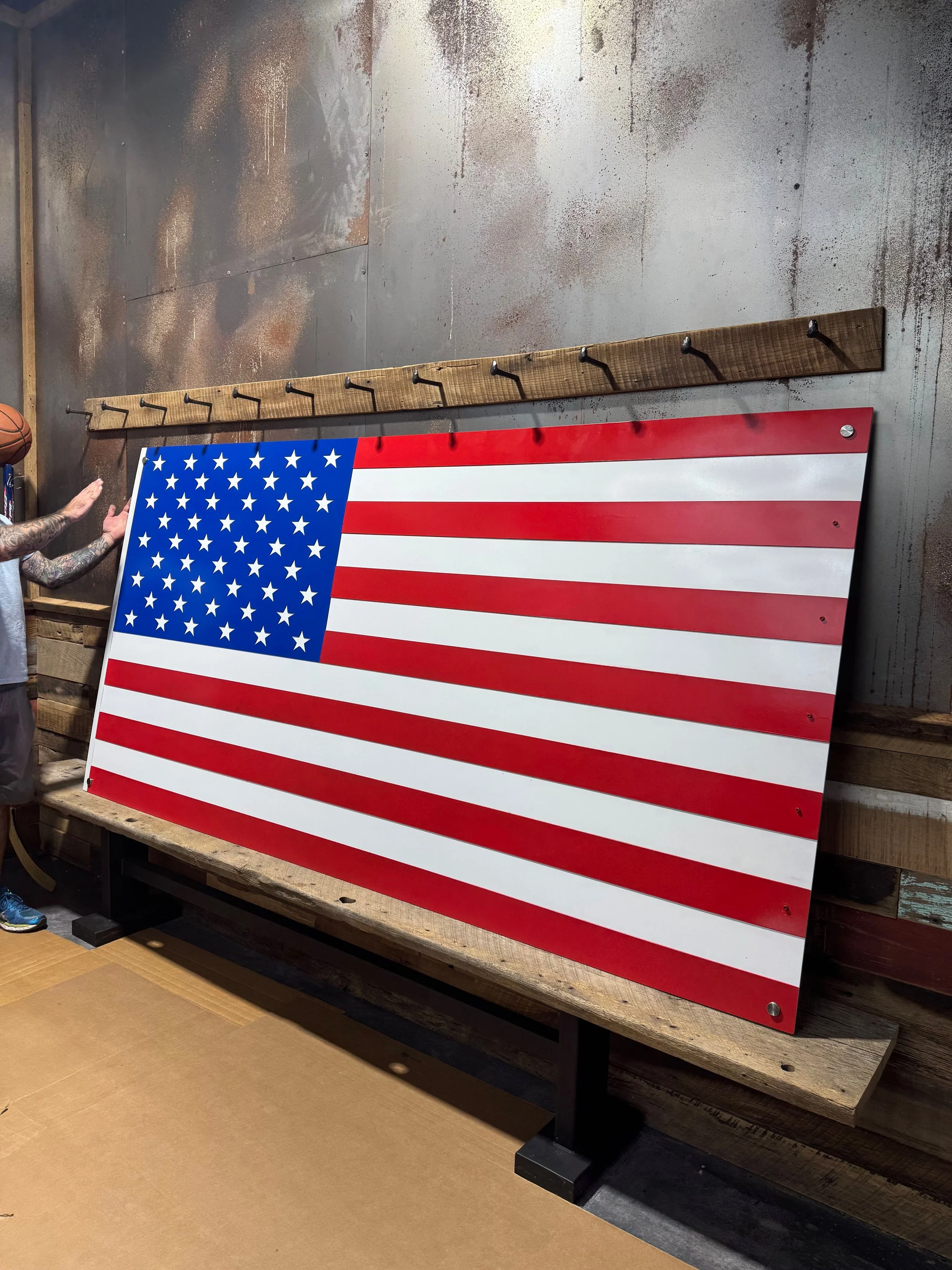 Large American flag decoration leaning against a wall, mounted on a wooden stand with hooks above.