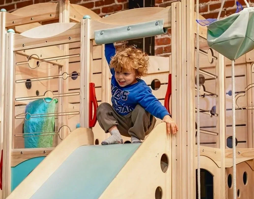 Toddler climbing the wooden play structure at Art Play Café.