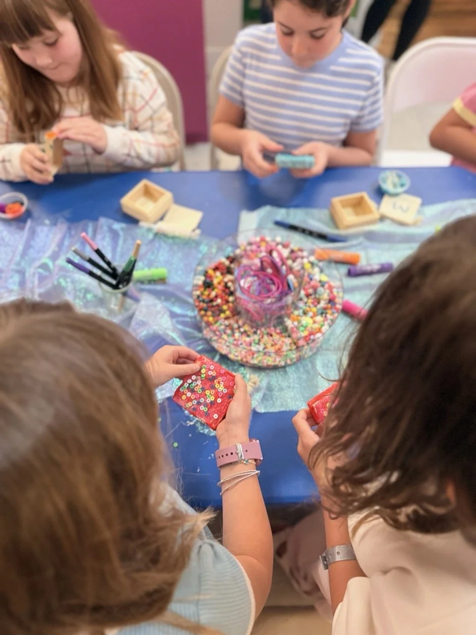 Kids adding sequins and beads to decorate boxes at a birthday party