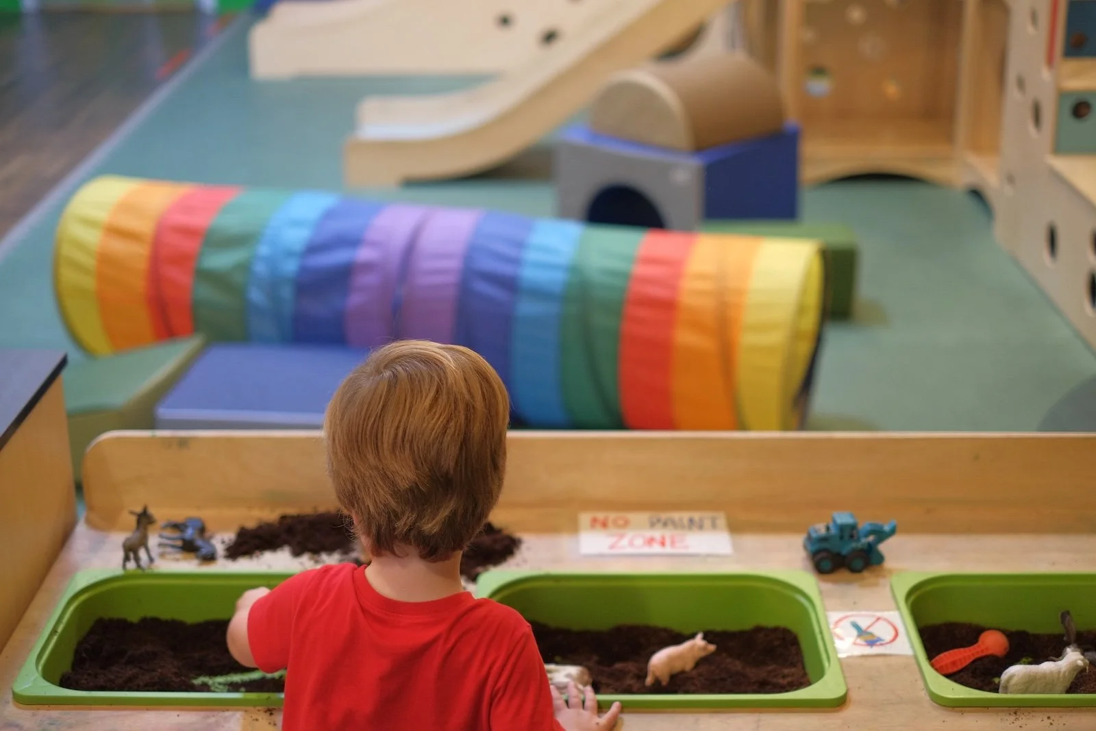 Child exploring a sensory play table with dirt and toy farm animals in the play room