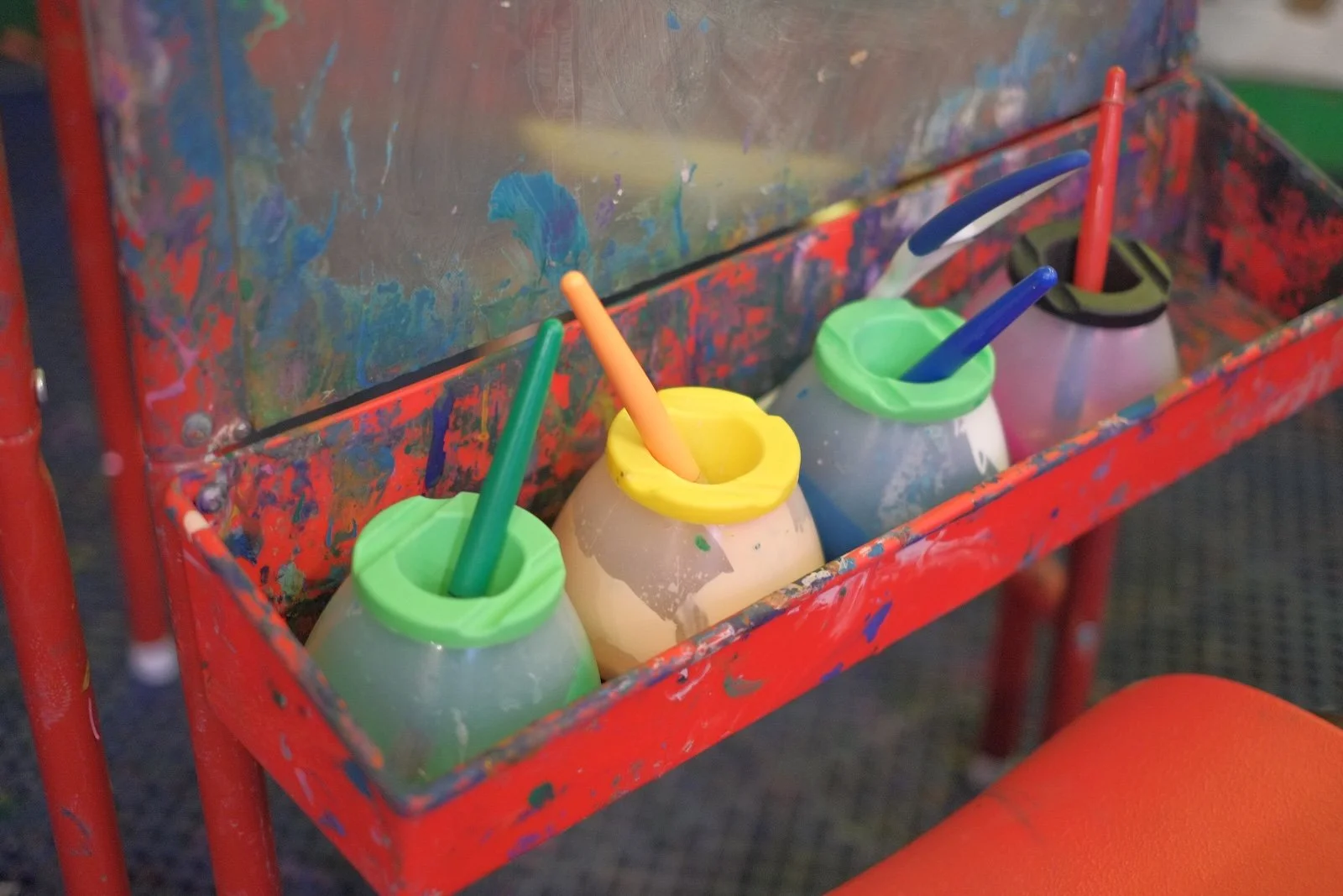 Paint station stocked with colorful paint cups and brushes for open art play