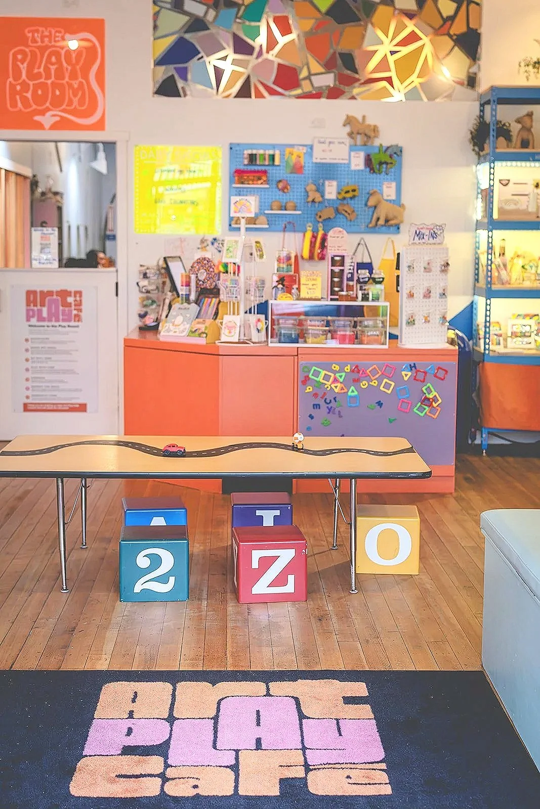 Check-in counter at Art Play Café with a 'Welcome to the Club' sign and entrance to the playroom.