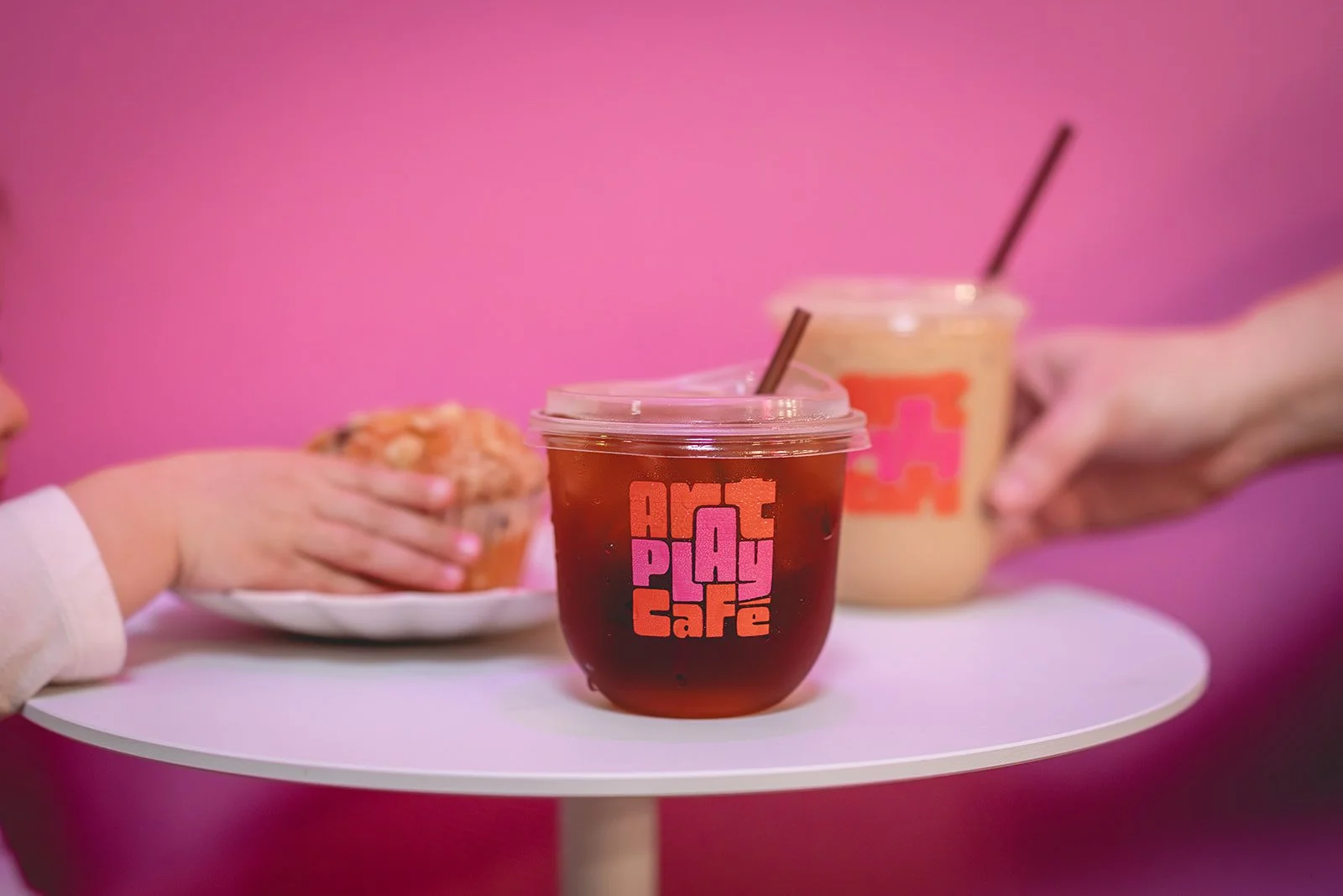 Iced coffee in an Art Play Café branded cup with a muffin at a café table