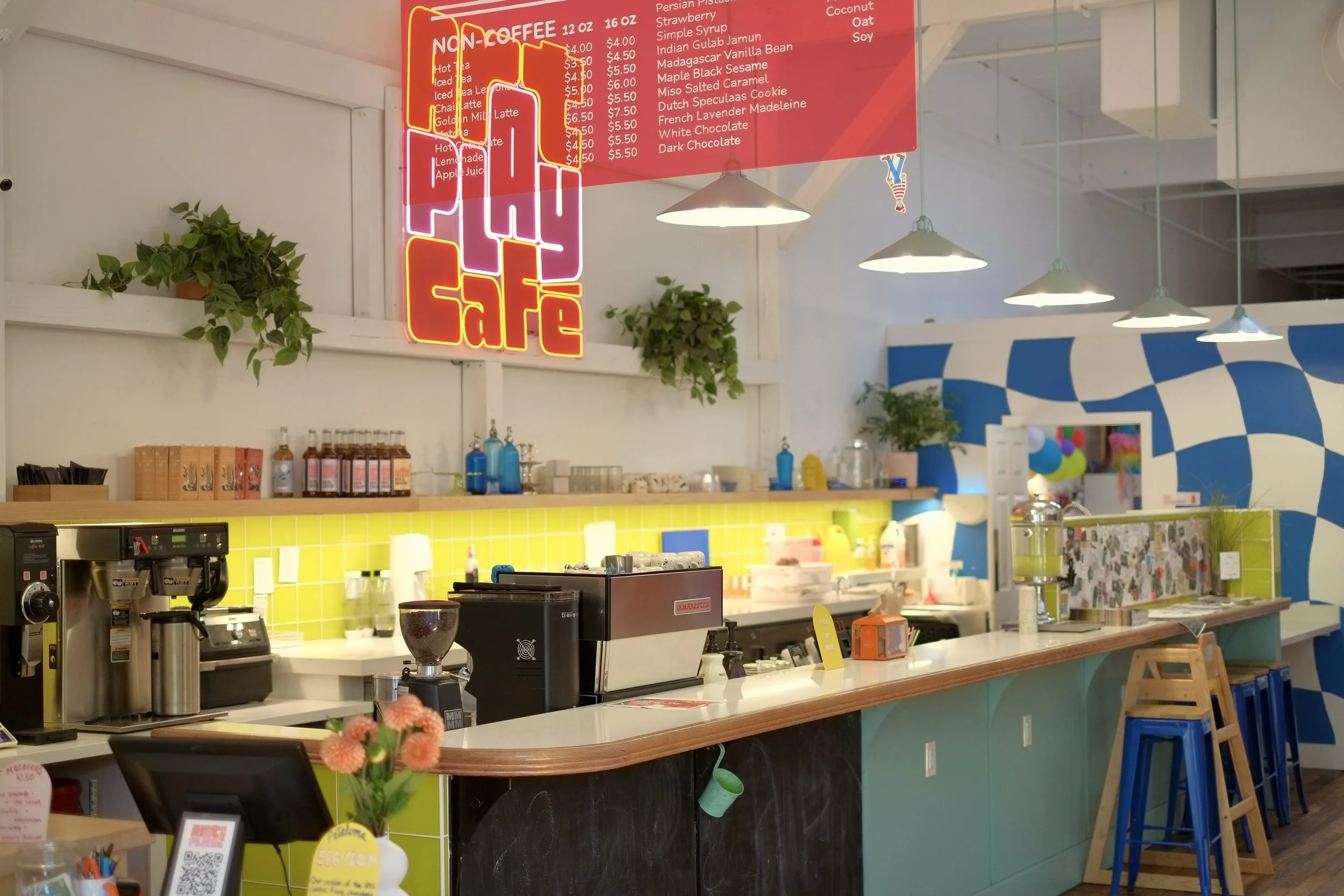 Espresso bar counter at Art Play Café with neon Play Café sign and drink menu board.