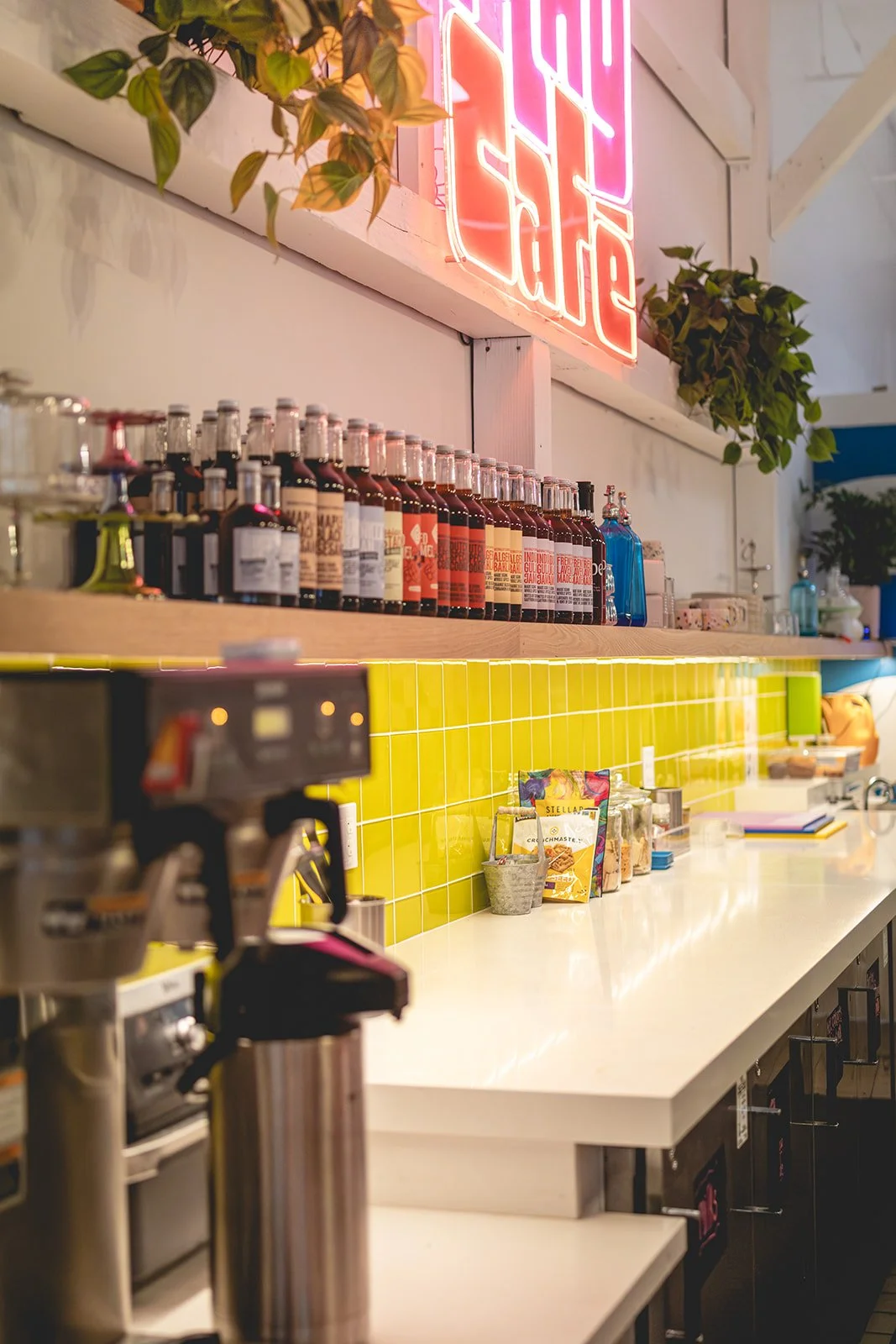 Neon café sign above a shelf of Transcendence syrups at Art Play Café