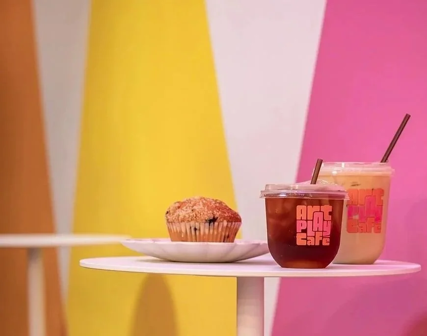 Colorful geometric mural on the wall at Art Play Café in Petaluma, with a muffin and two drinks in the foreground.