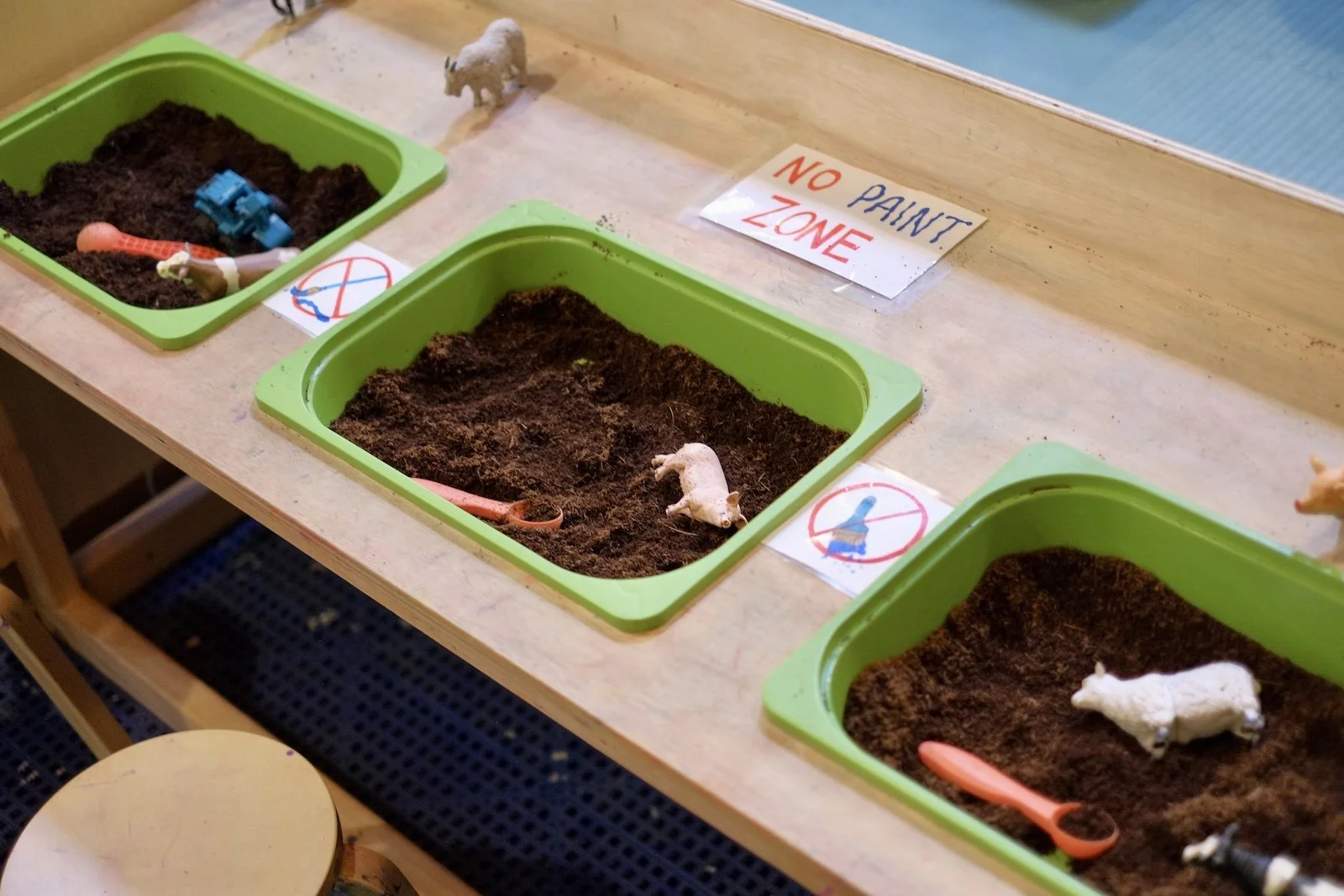 Sensory play bins filled with pretend dirt and toy animals on the play room activity table