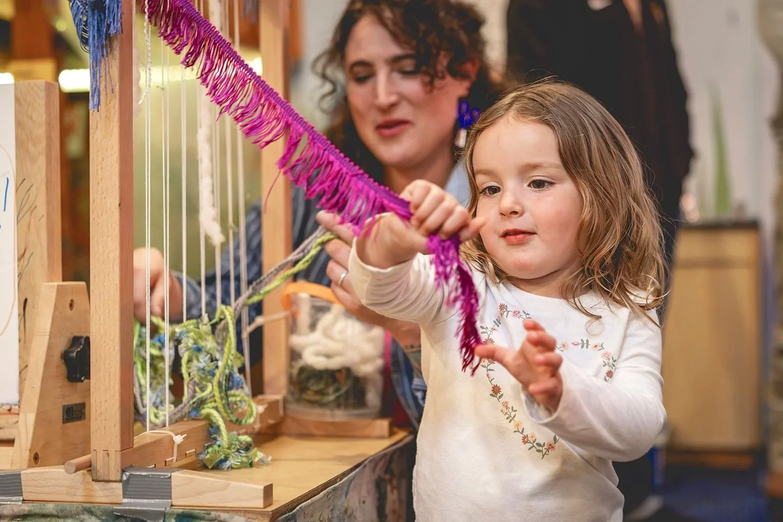 Child weaving colorful yarn on a loom with help from an adult