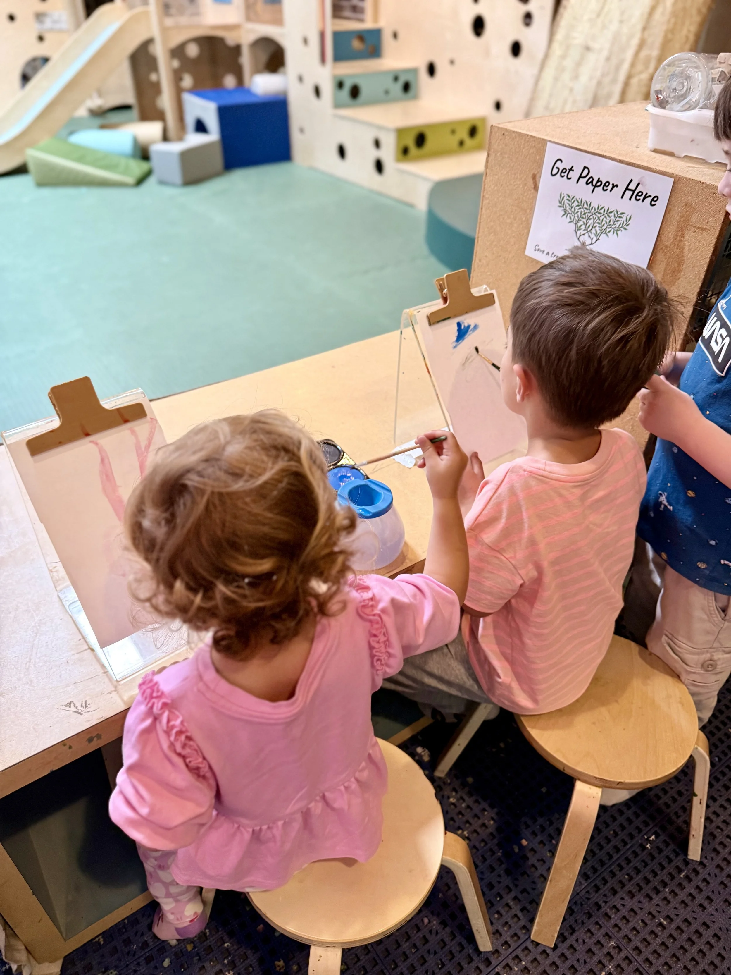 wo children doing art at Art Play Café, with the play structure visible in the background.