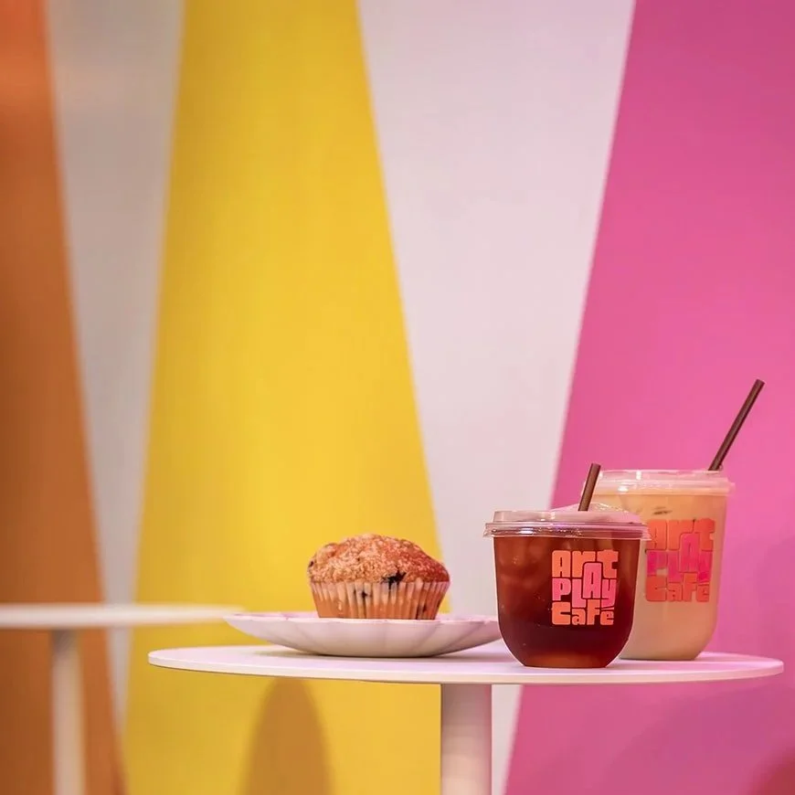 Colorful geometric mural on the wall at Art Play Café in Petaluma, with a muffin and two drinks in the foreground.