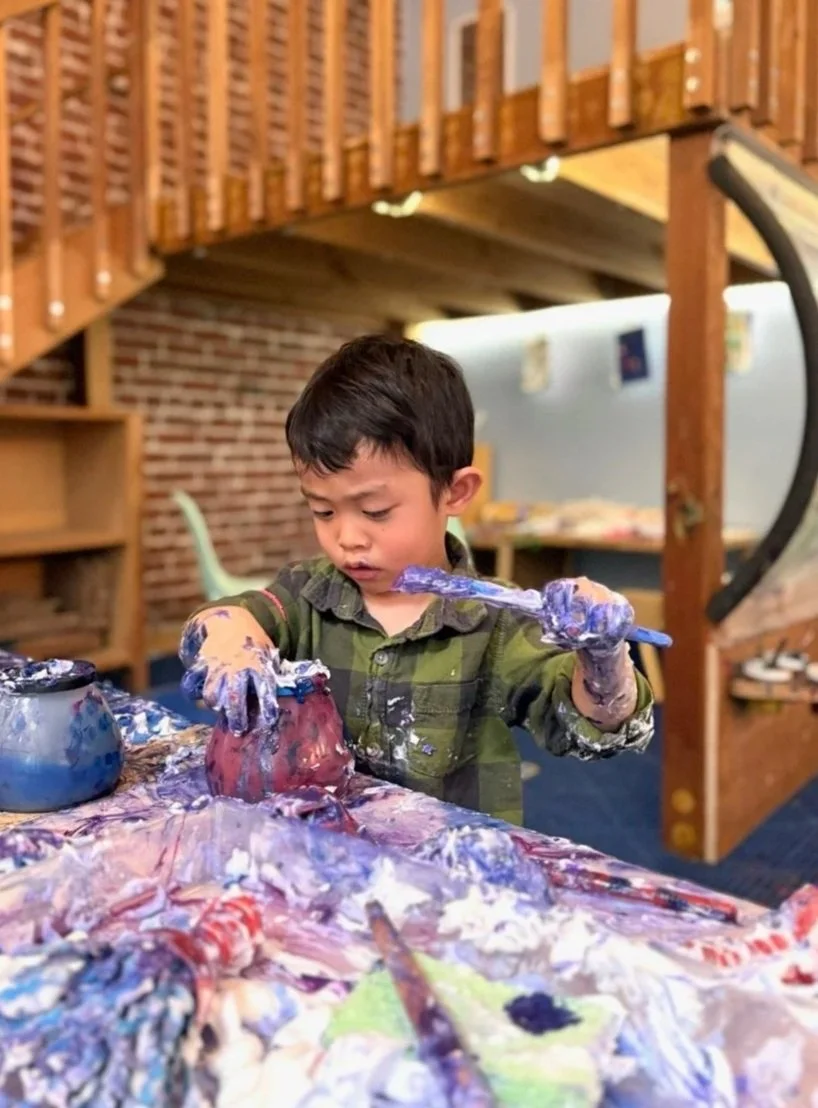 Child fully immersed in a hands-on painting activity at the art table