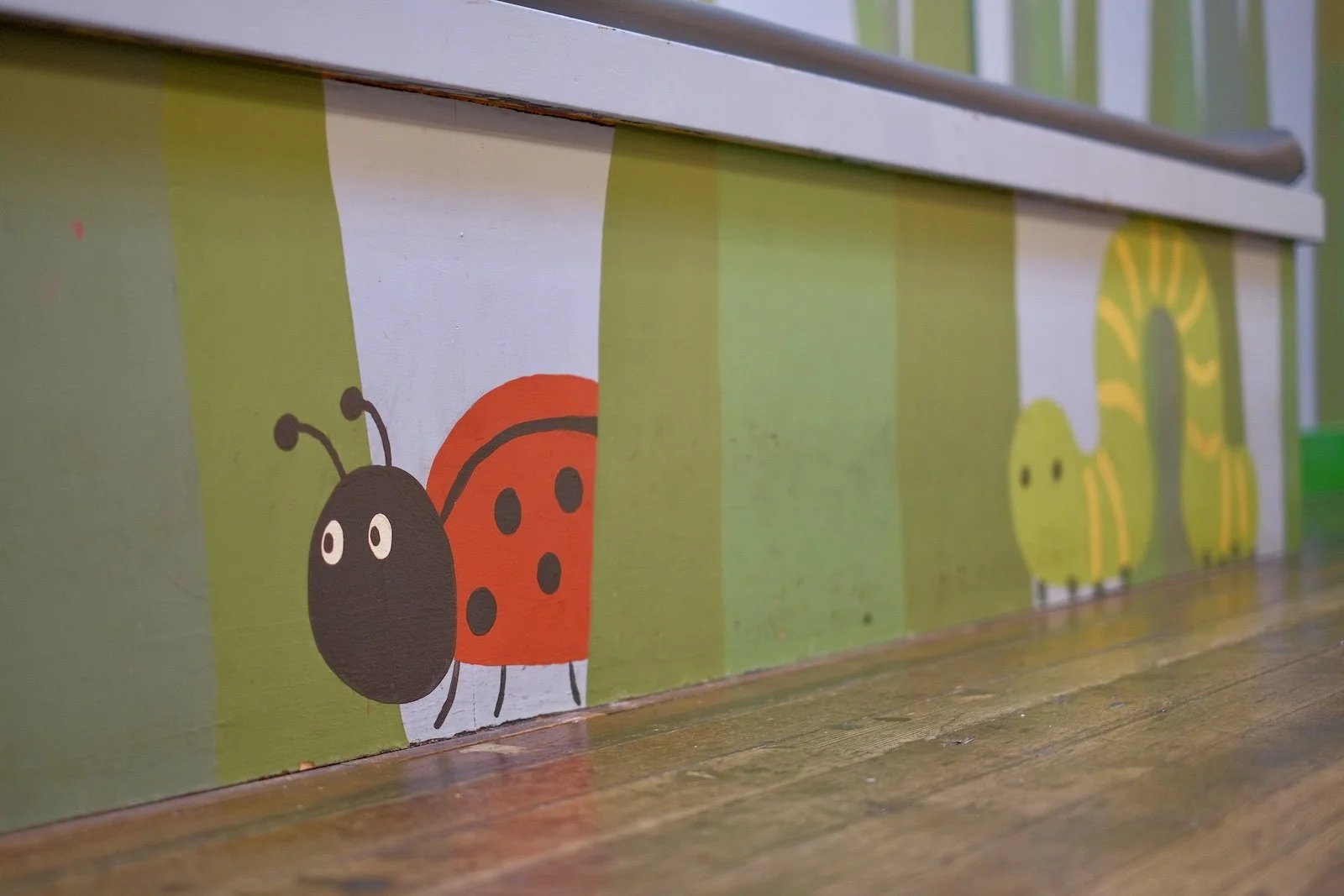 Hand-painted grass mural with a ladybug and caterpillar design along the play room wall