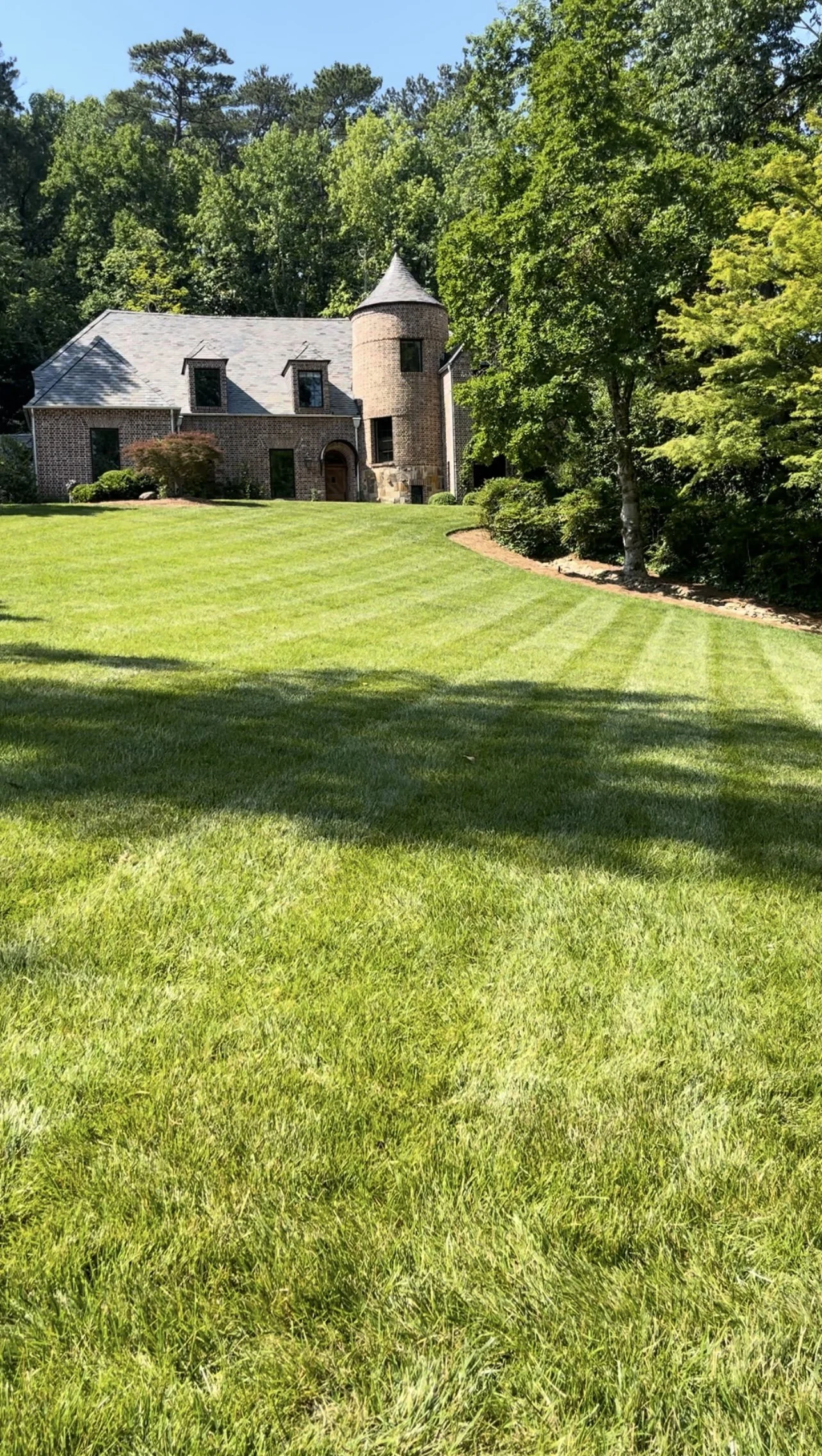 A large brick house with a round turret, surrounded by lush green trees and a well-manicured lawn.