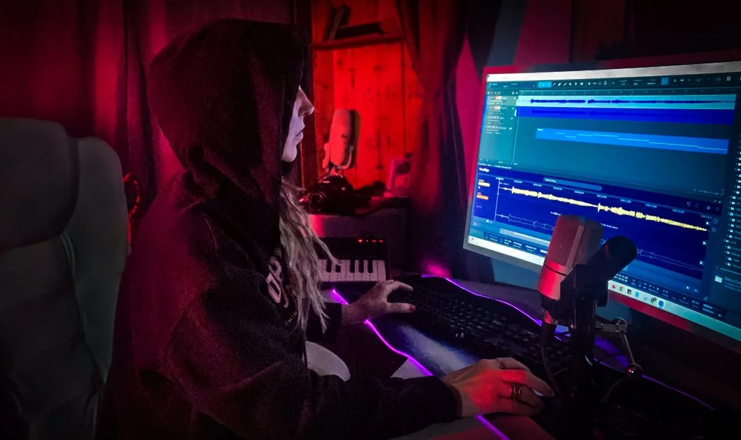 Christine Greyson working in her home studio, hood up, mixing in Studio One with a waveform glowing on screen