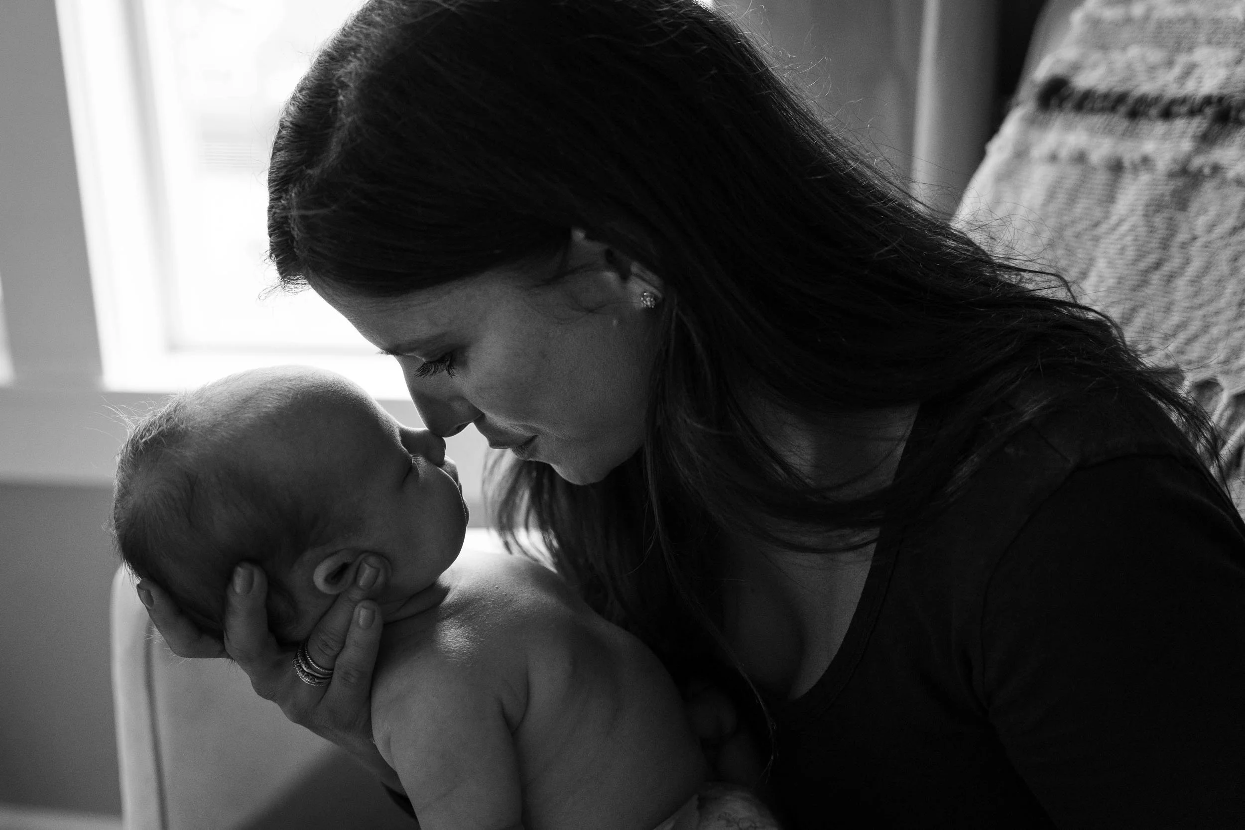 Left: Black-and-white portrait of a mother touching noses with her newborn beside a bright window during a newborn photography shoot in Bellevue.