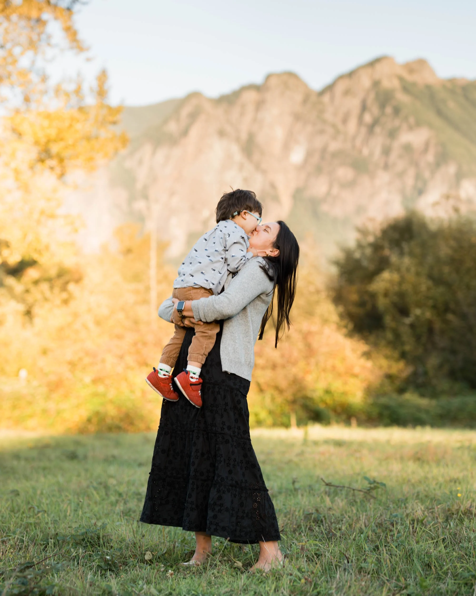 An adventurous mom is holding up her 5 year old with Mt Si mountains behind her. 