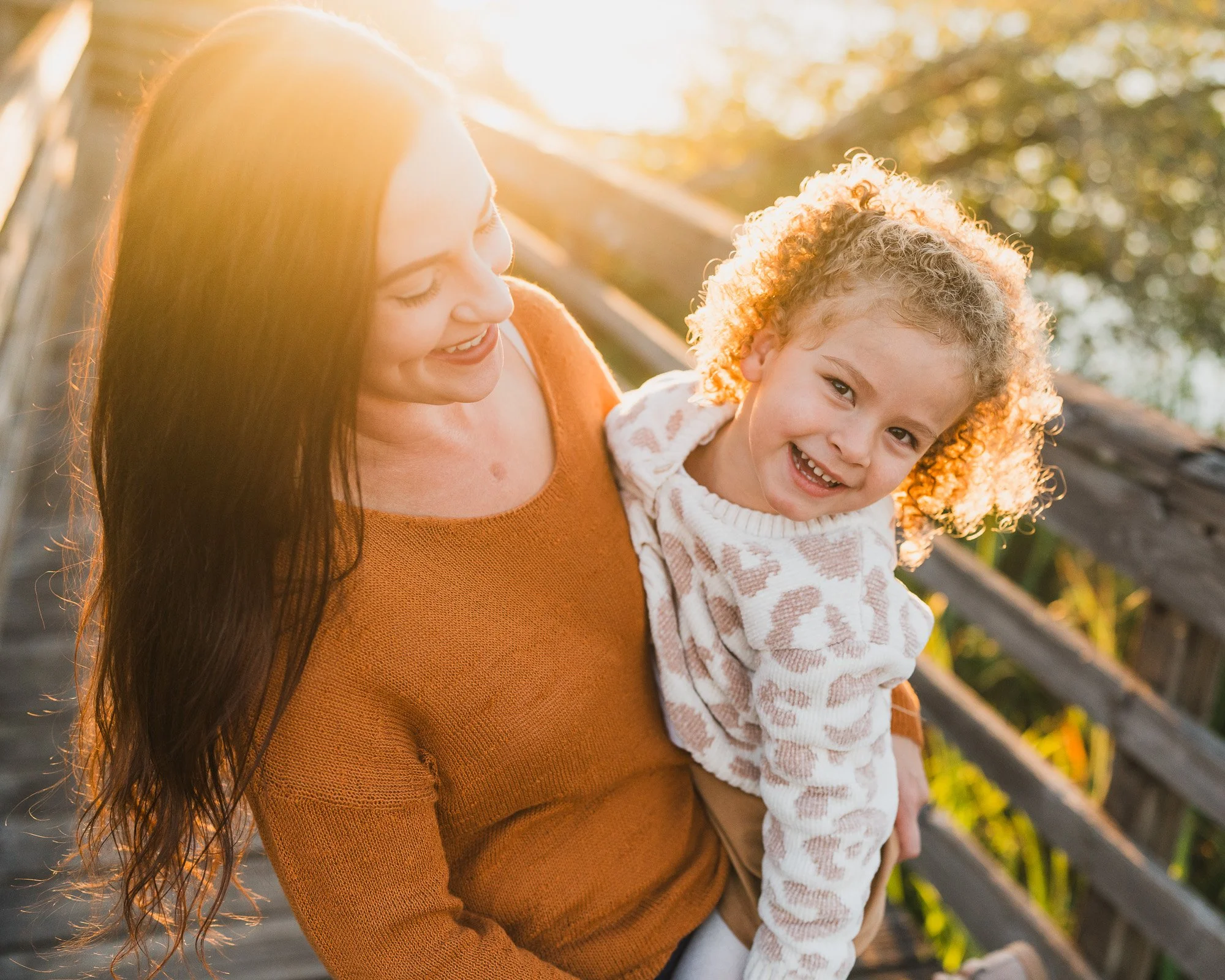 A mom is laughing at golden hour while holding her 4 year old at Juanita Bay park.