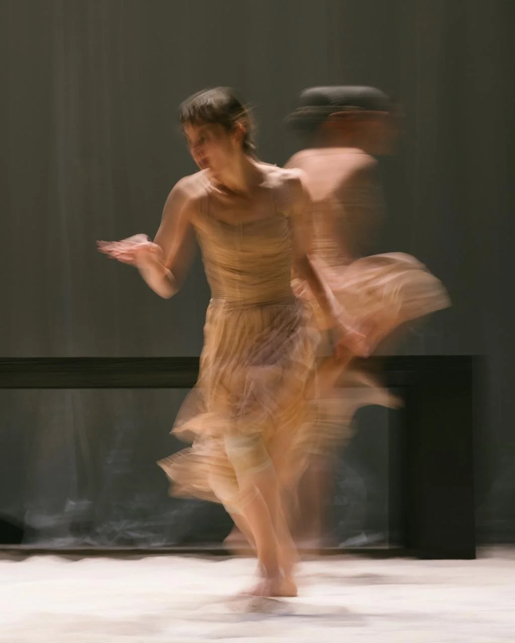 A woman spinning and dancing in a flowing dress with blurred motion, on a stage with a dark background.